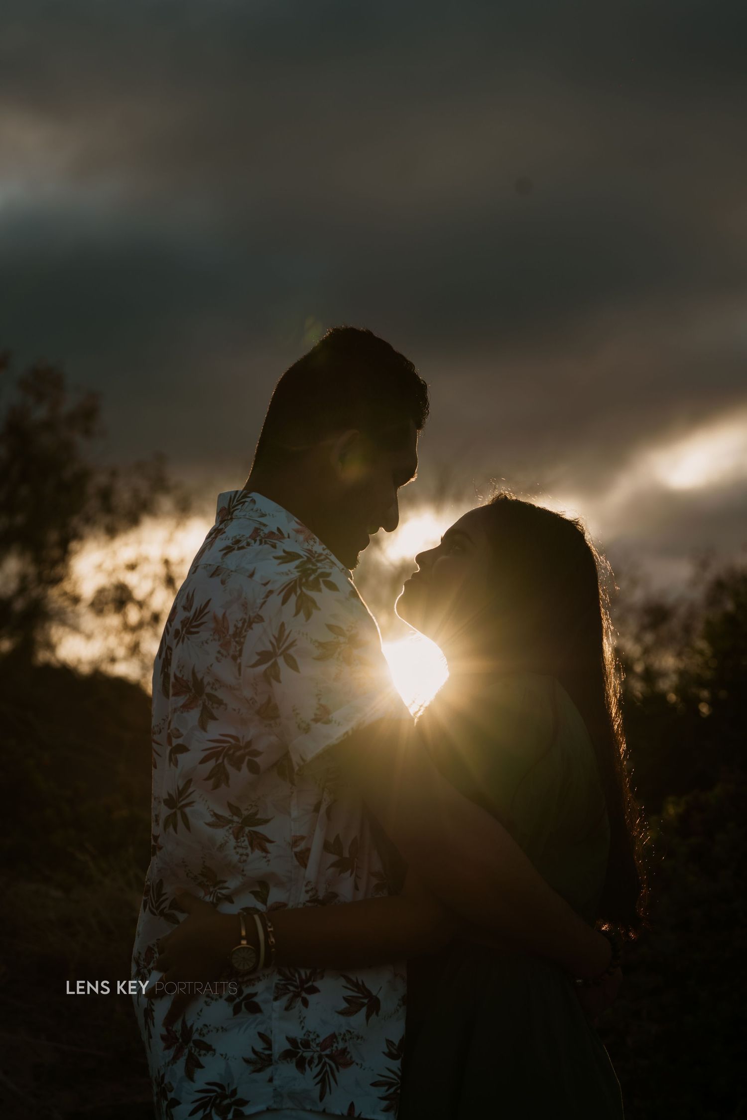 Romantic silhouette of a couple nearly kissing against a dramatic golden sunset with lens flare.