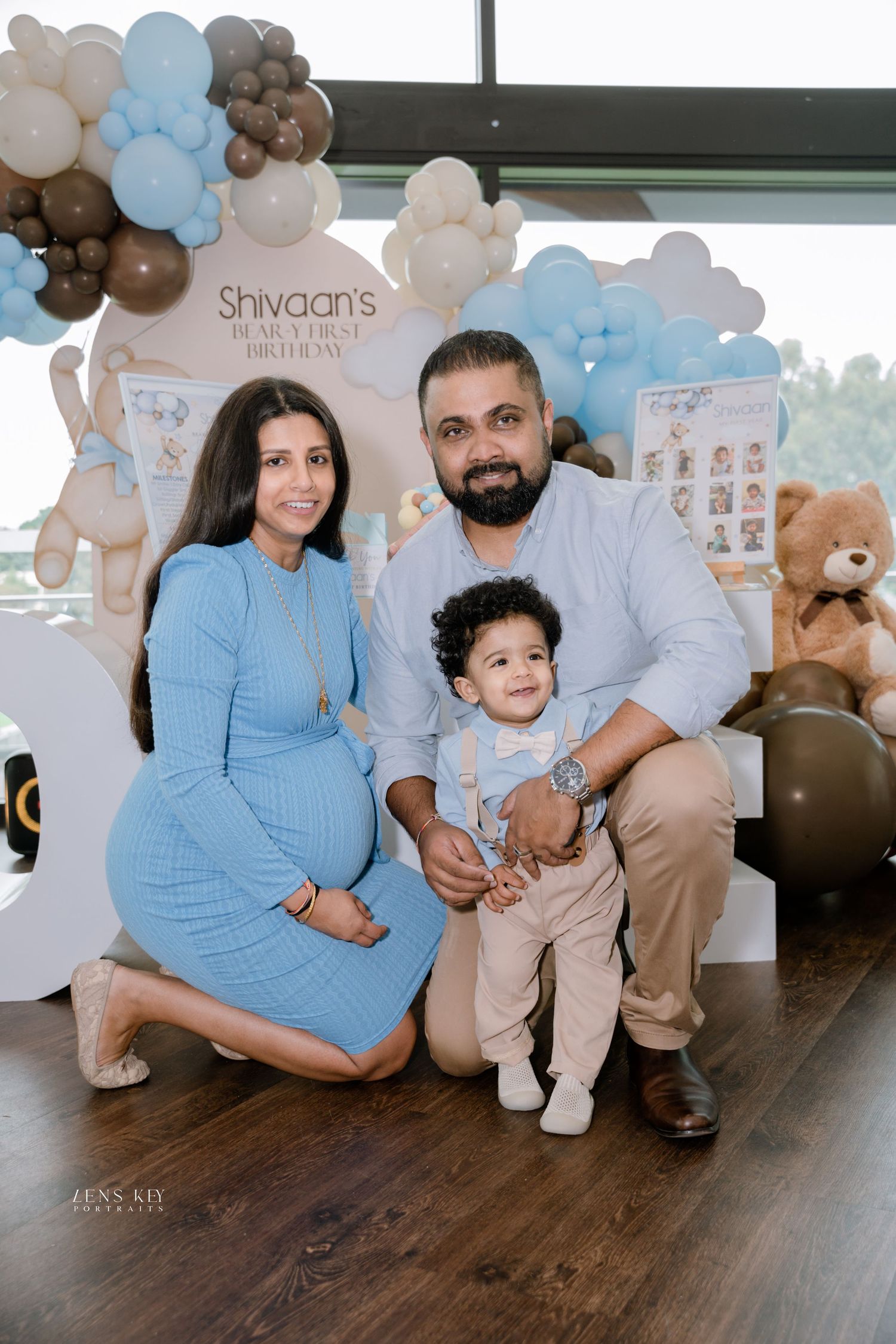 Family portrait at Shivaan's first birthday party with blue balloon garland backdrop.