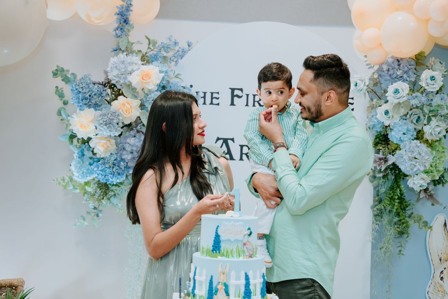 Parents and baby boy celebrate first birthday cutting cake at Peter Rabbit themed party.