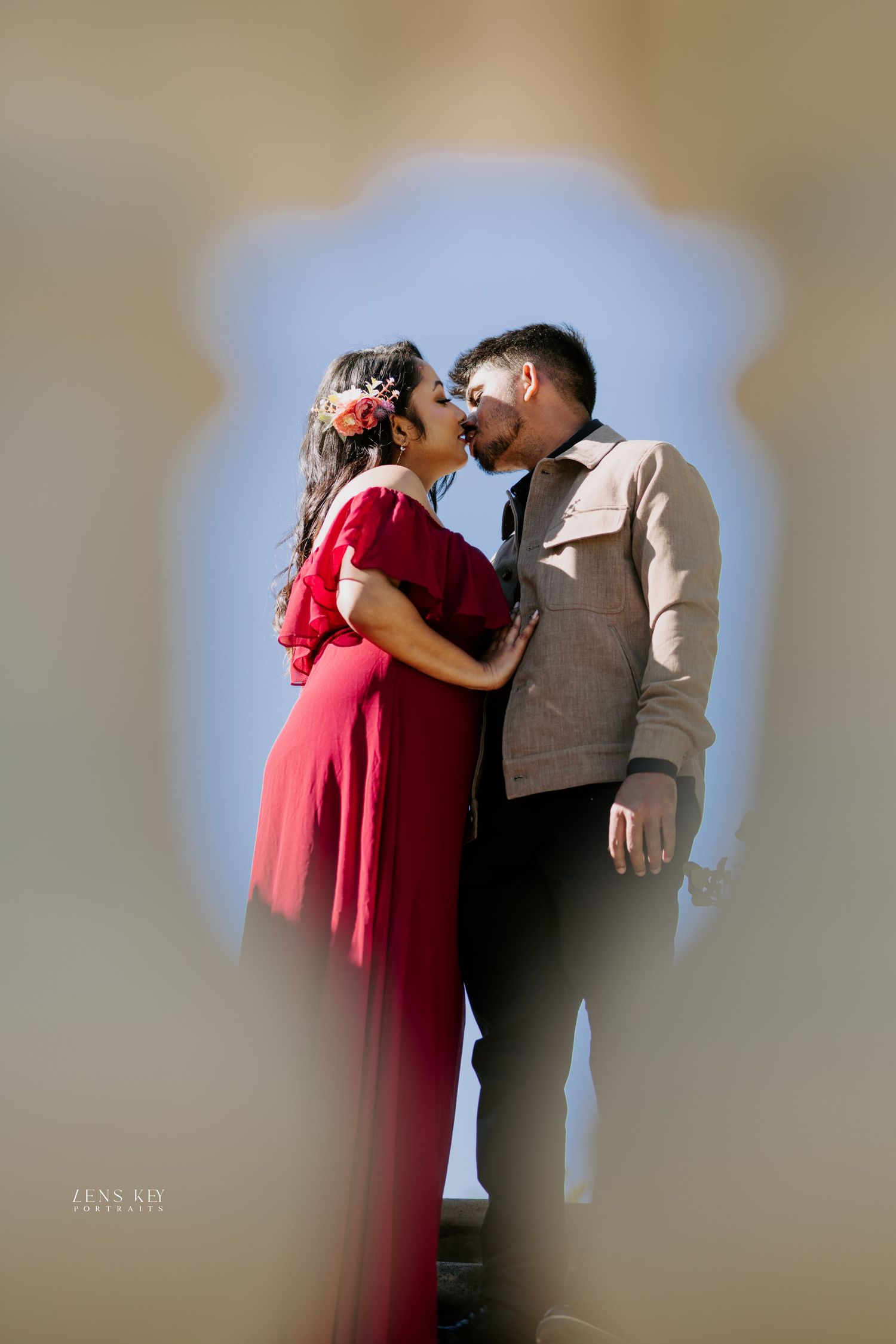 Couple sharing a kiss framed through a decorative keyhole-shaped architectural opening.