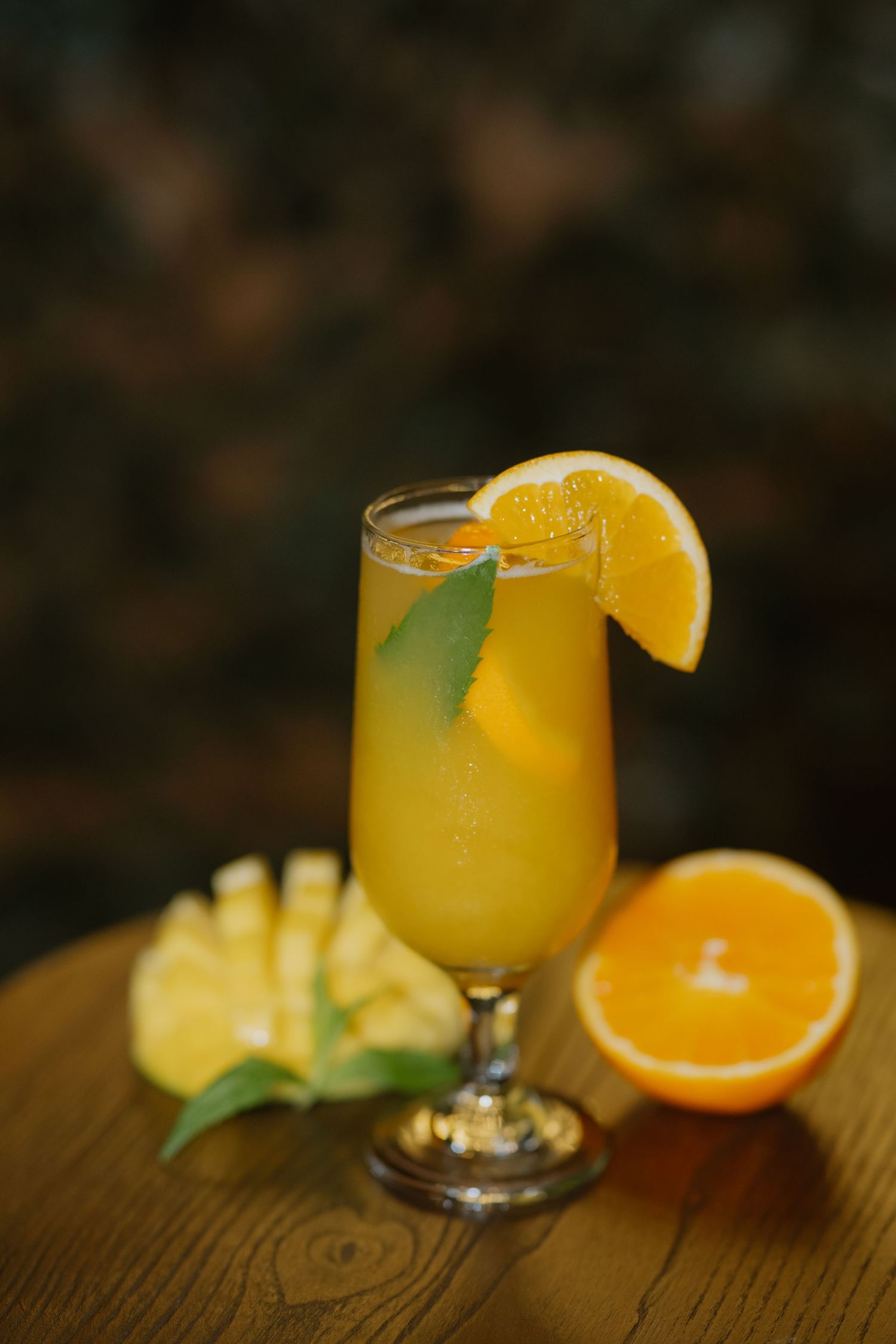 Orange pineapple tropical cocktail garnished with fresh orange slice and mint leaf in stemmed glass.