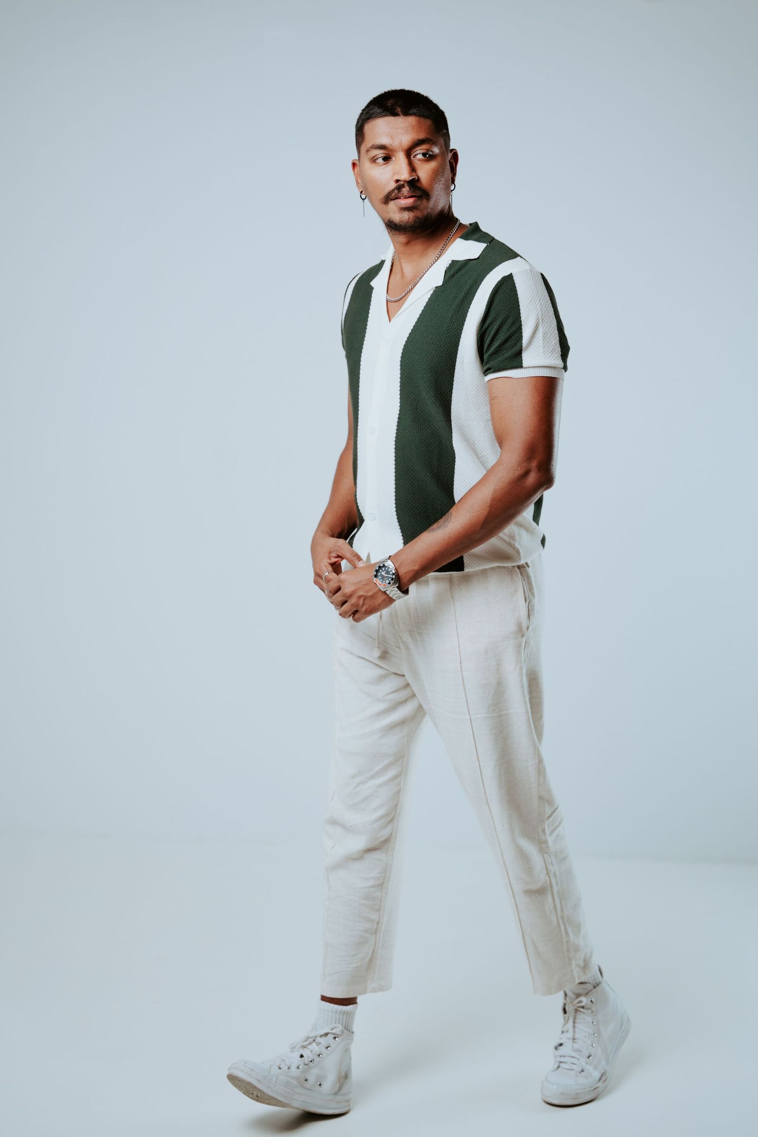 Stylish man in green and white striped polo shirt and cream pants poses in studio.