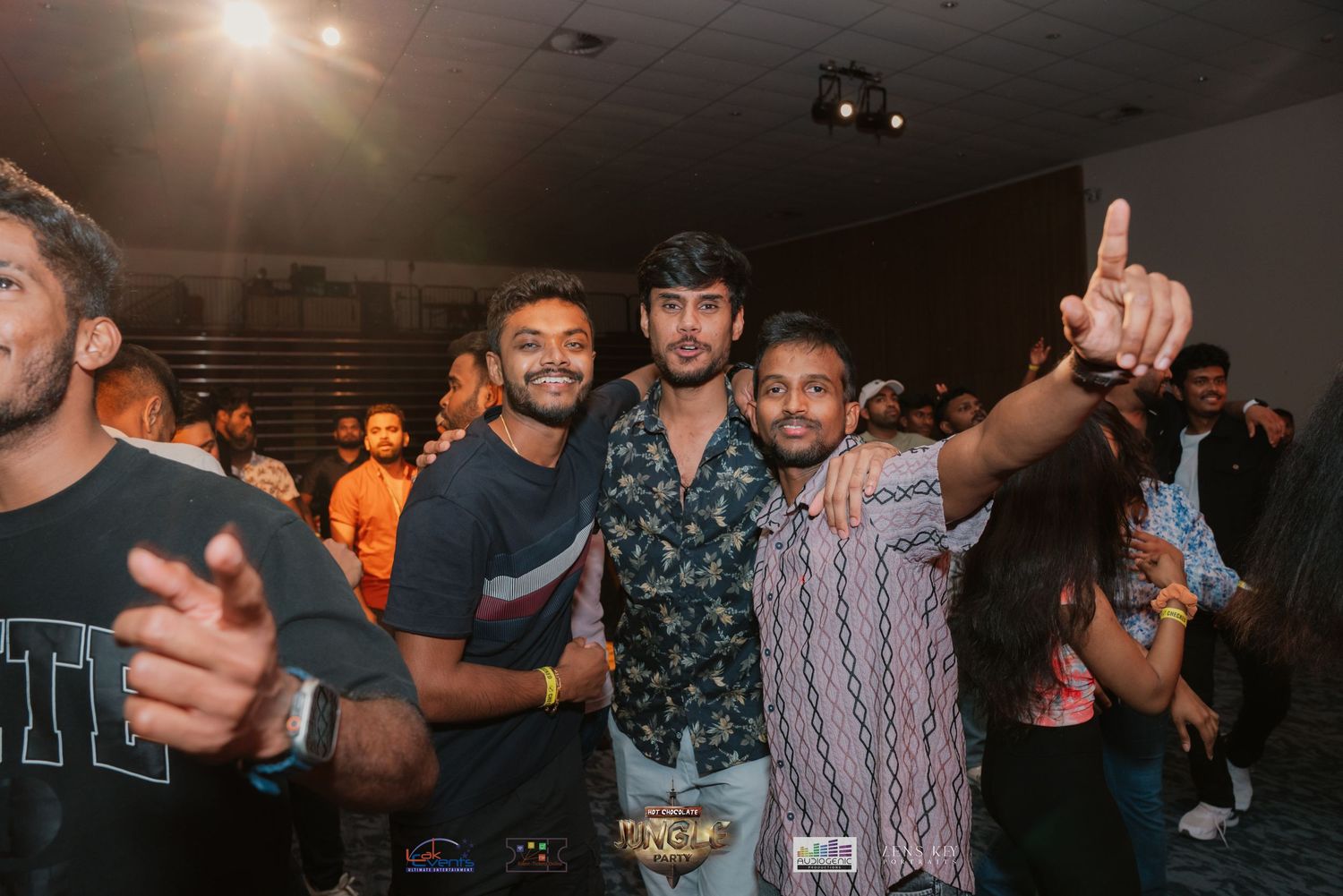 Three young men posing together and smiling at a live music event.