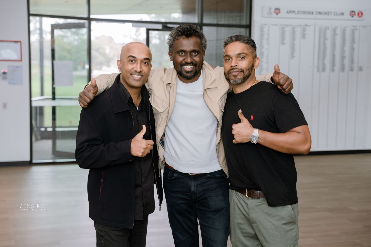 Three men smiling and giving thumbs up at an indoor cricket club event.