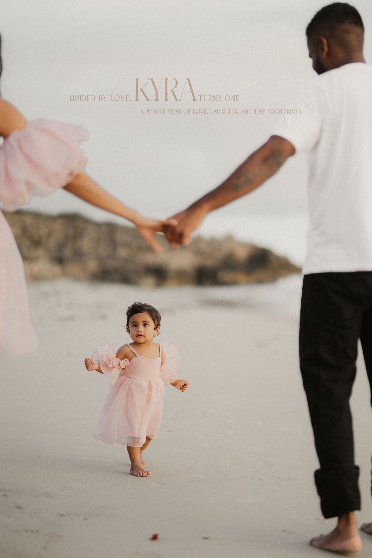 Baby girl in pink dress walking between parents holding hands on beach.