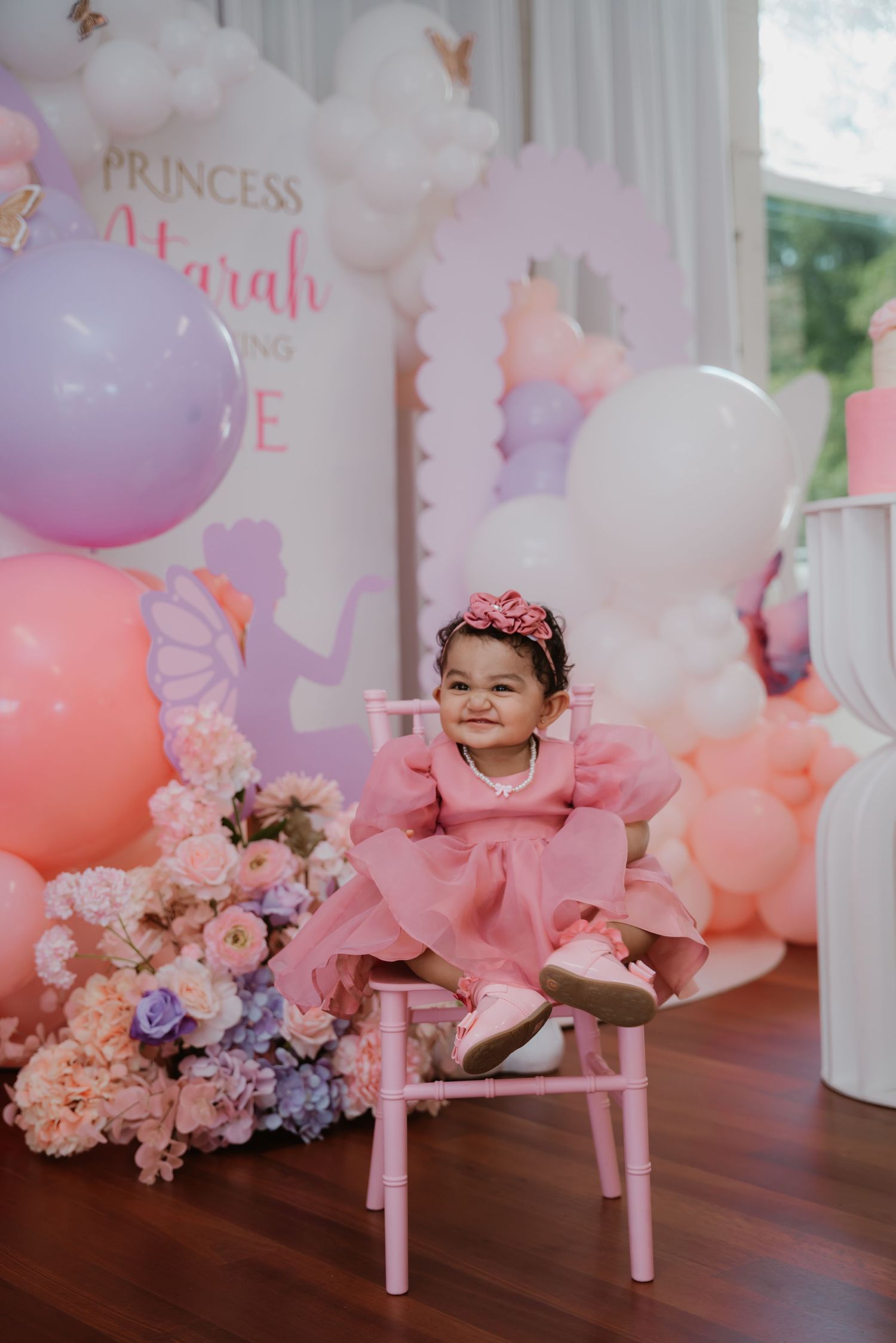 Baby girl in pink tulle dress sitting on chair at Princess Atarah first birthday party.