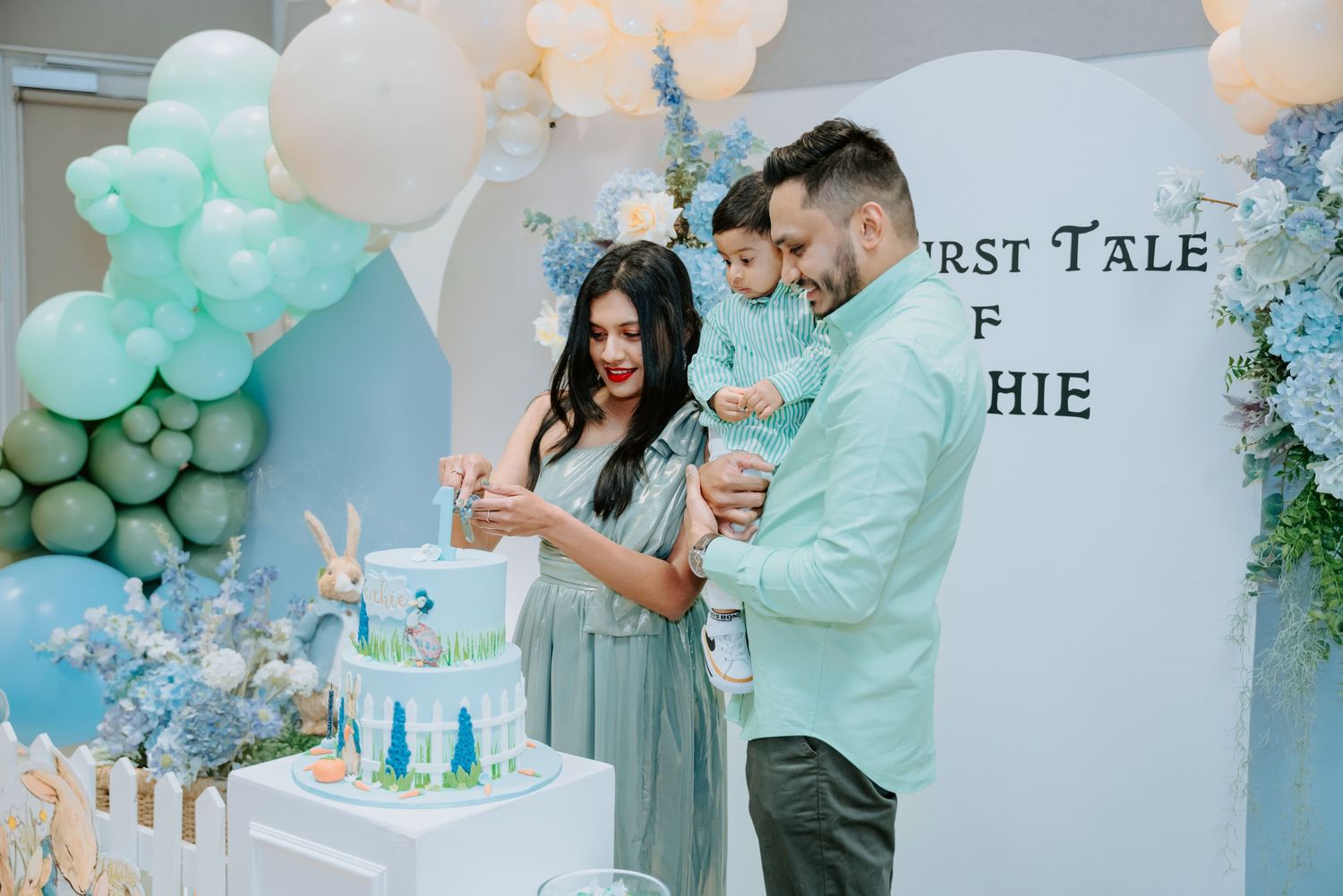 A couple cuts a decorated cake at an elegant blue Peter Rabbit themed first birthday party.