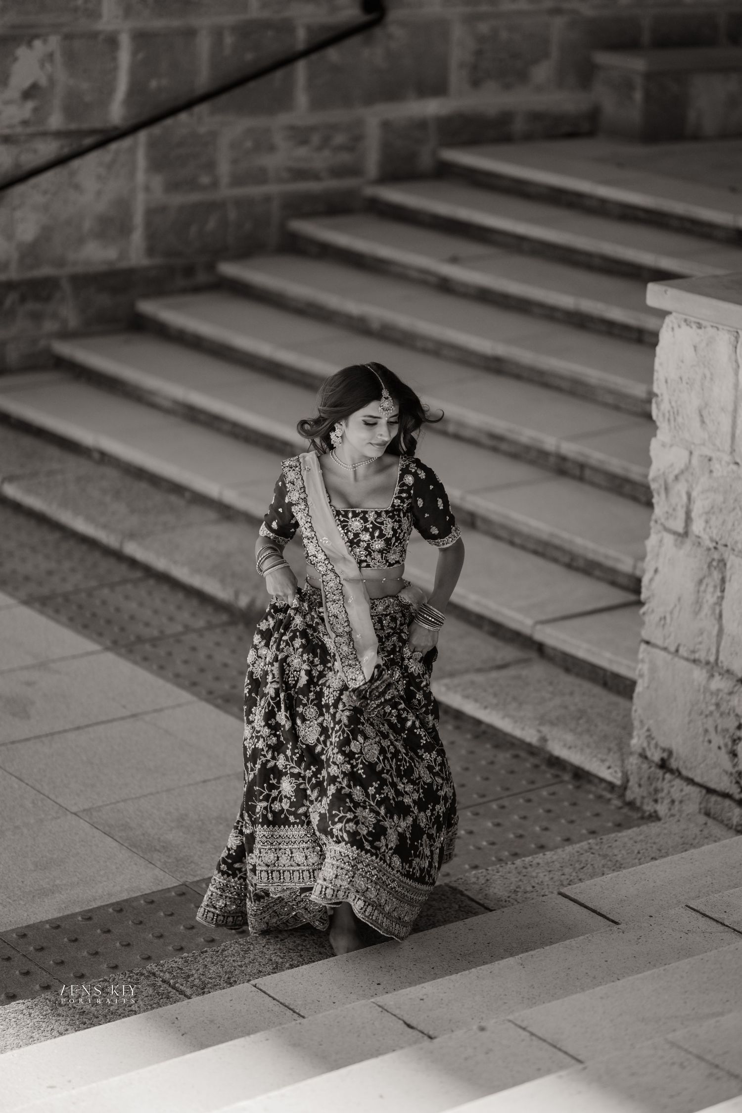 Black and white photo of woman in embroidered lehenga walking up stone steps.