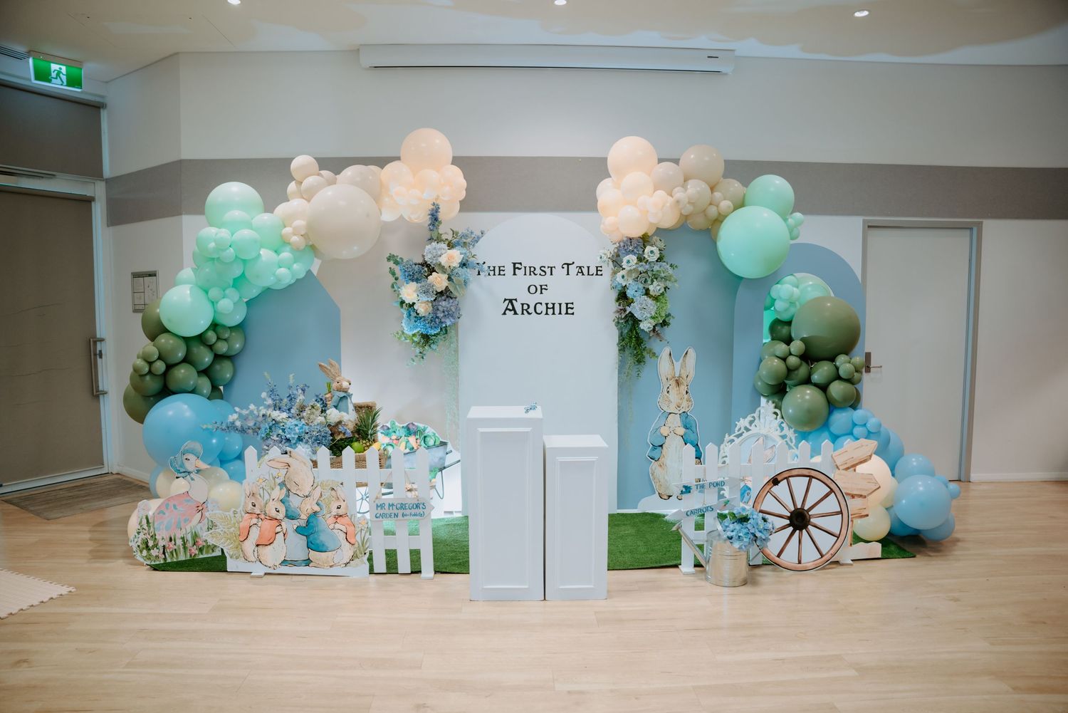 Peter Rabbit themed birthday party backdrop with blue balloon arch and white picket fence.