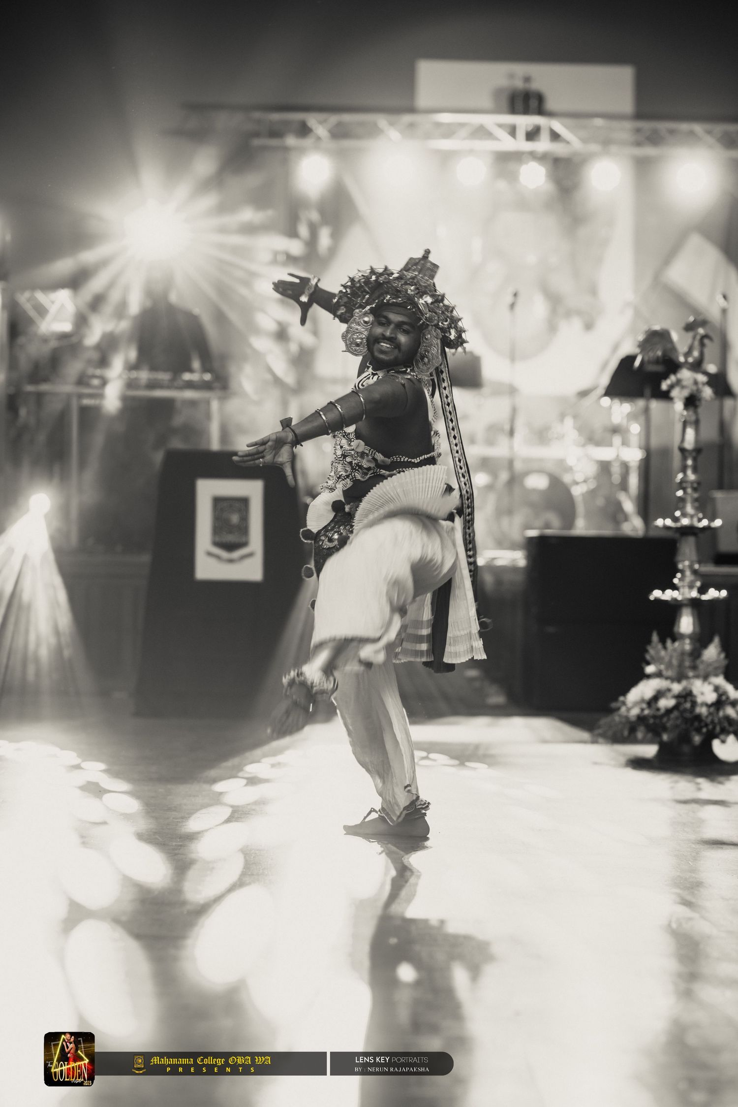 A traditional dancer performing on stage in costume under bright spotlights in black and white.