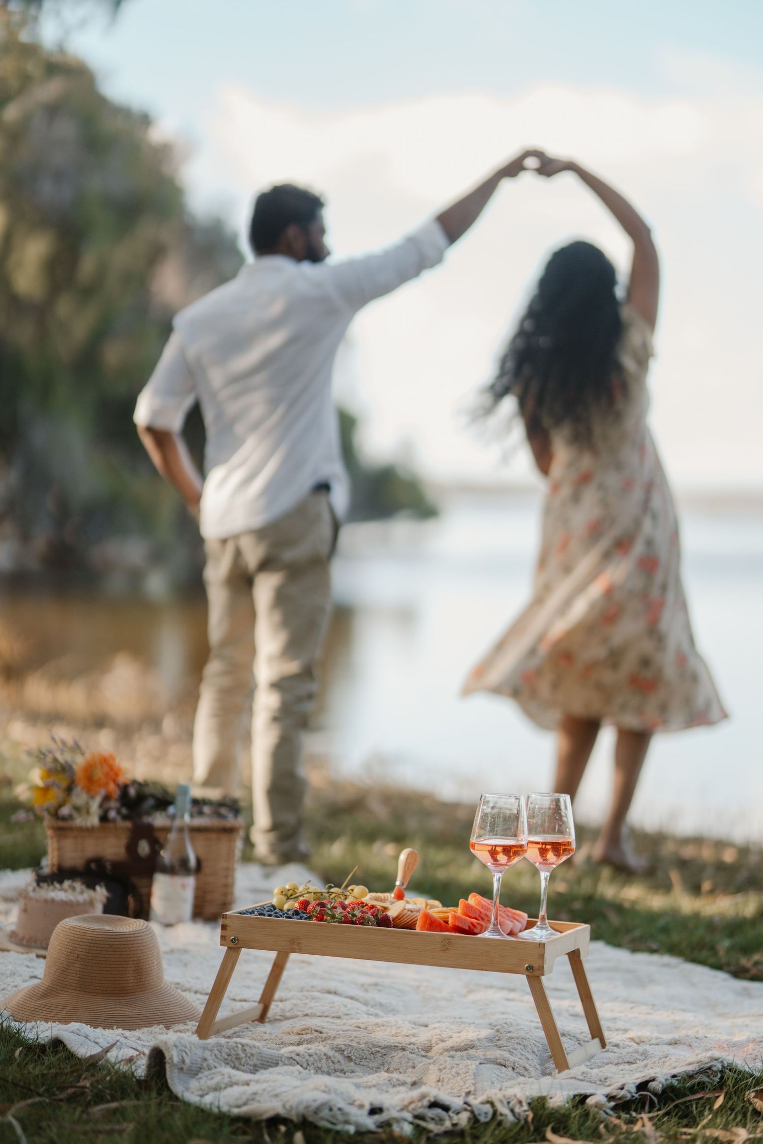 Couple dancing by lakeside with charcuterie board and rose wine in foreground.