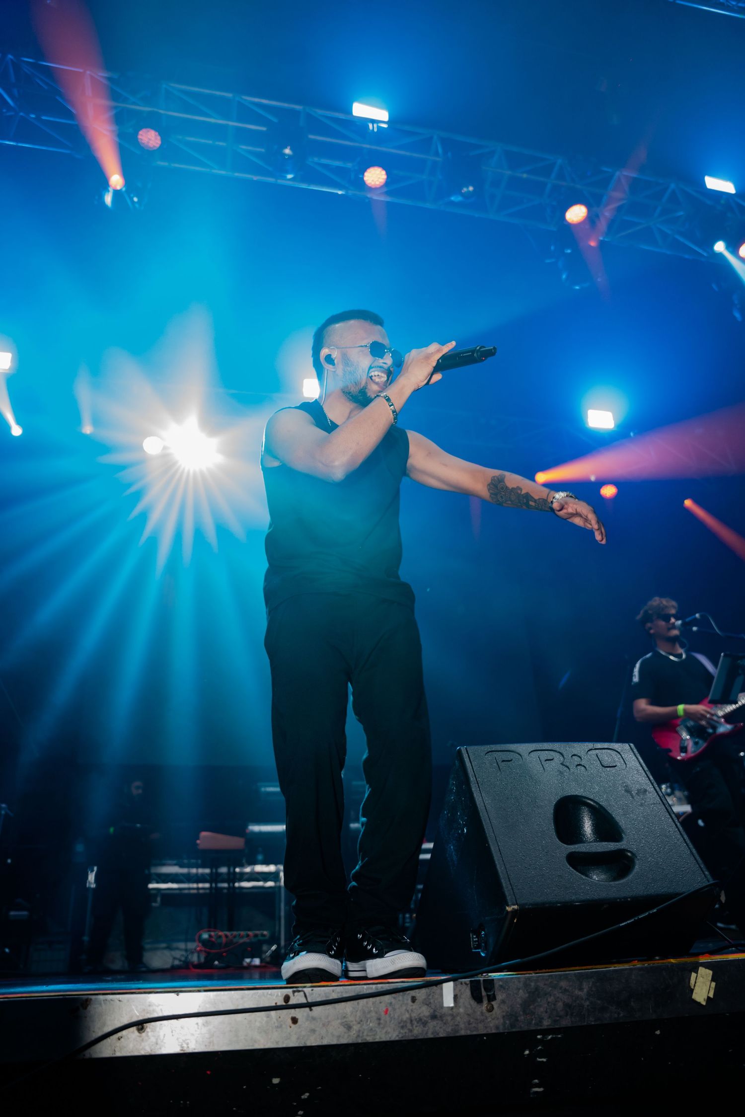 Male performer in black outfit sings on stage with dramatic blue stage lighting at concert.