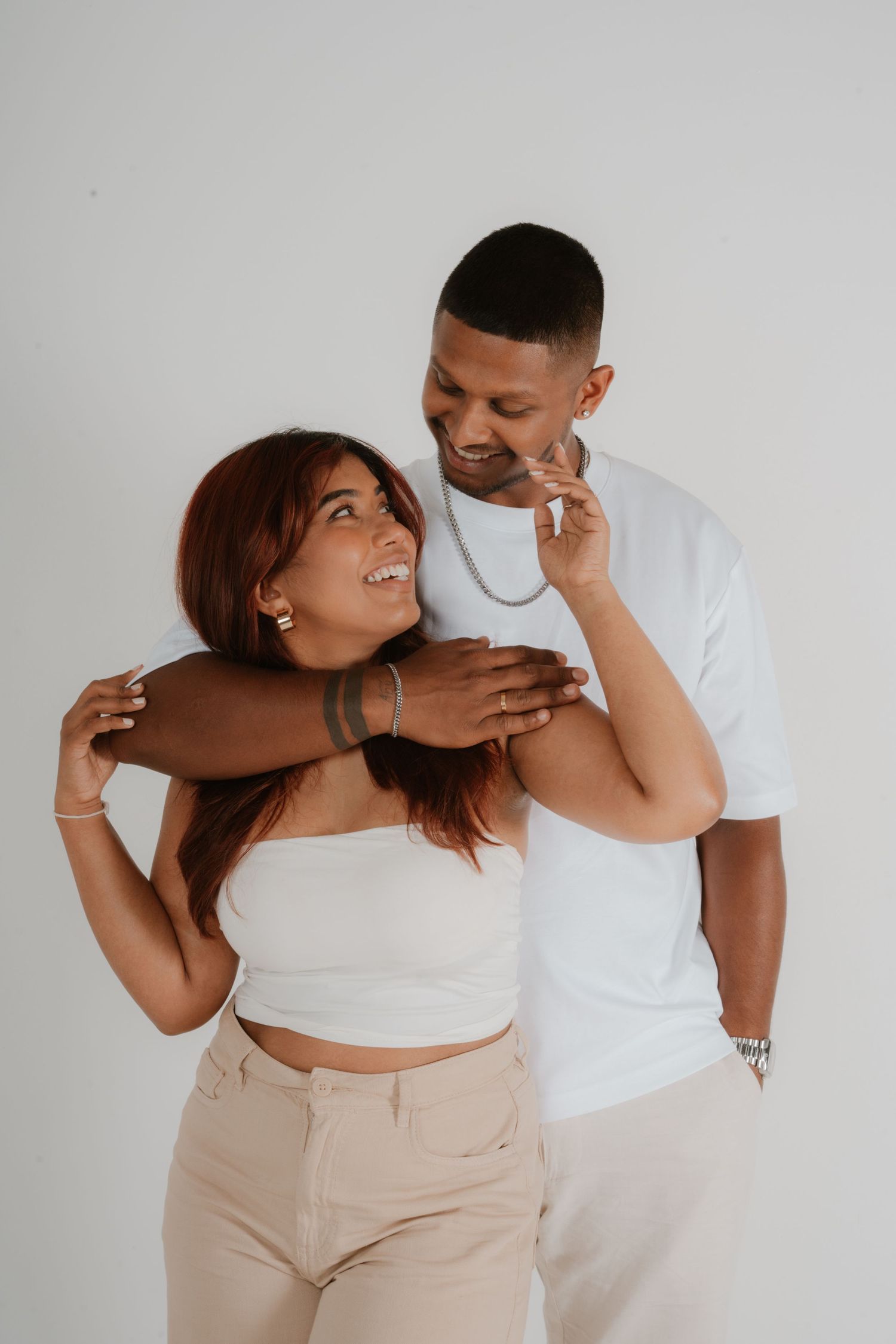 Man in white tee embracing woman in white crop top, both smiling in studio setting.