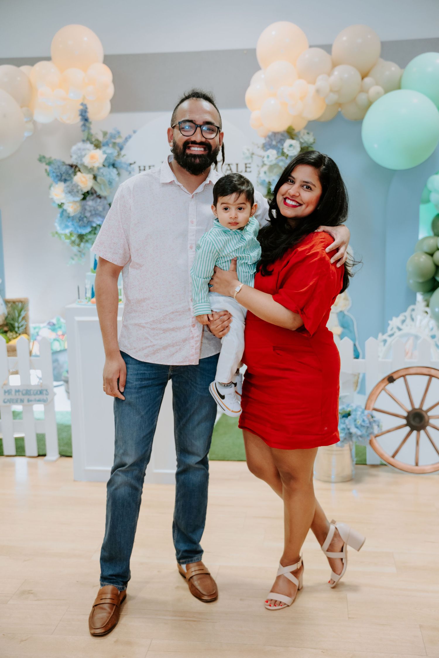 Family of three posing at a Peter Rabbit themed birthday party with balloon arch decor.