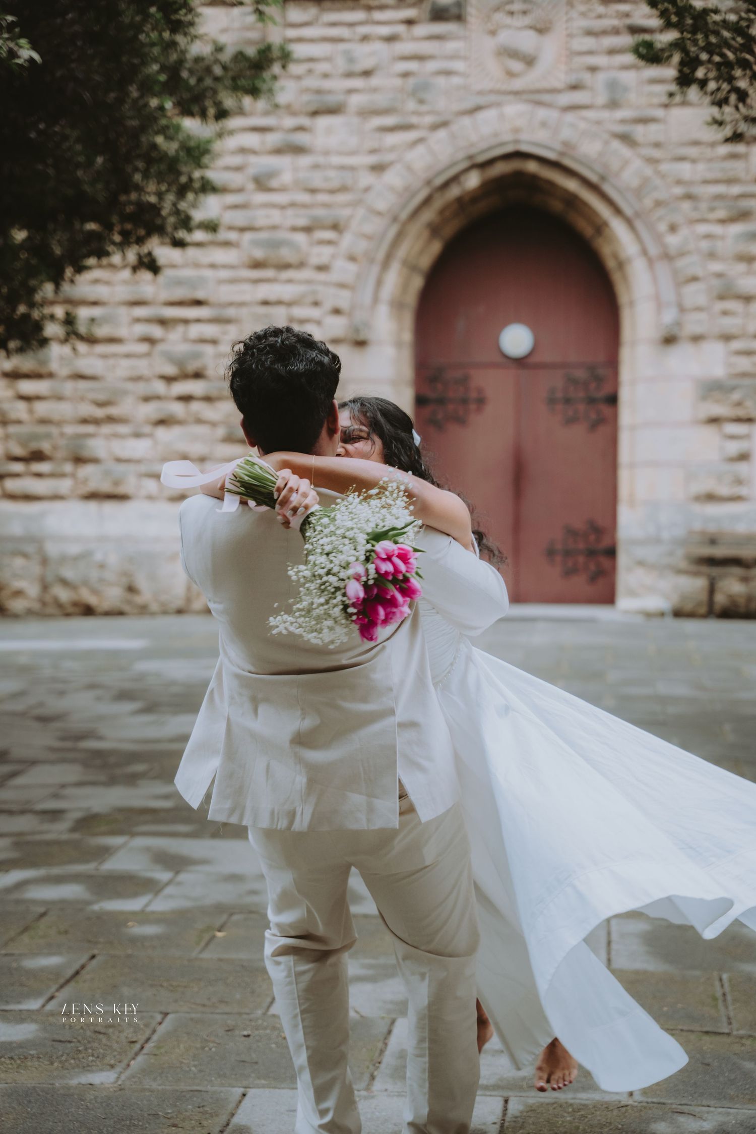 Bride and groom embracing outside historic stone church with flowing white wedding dress.