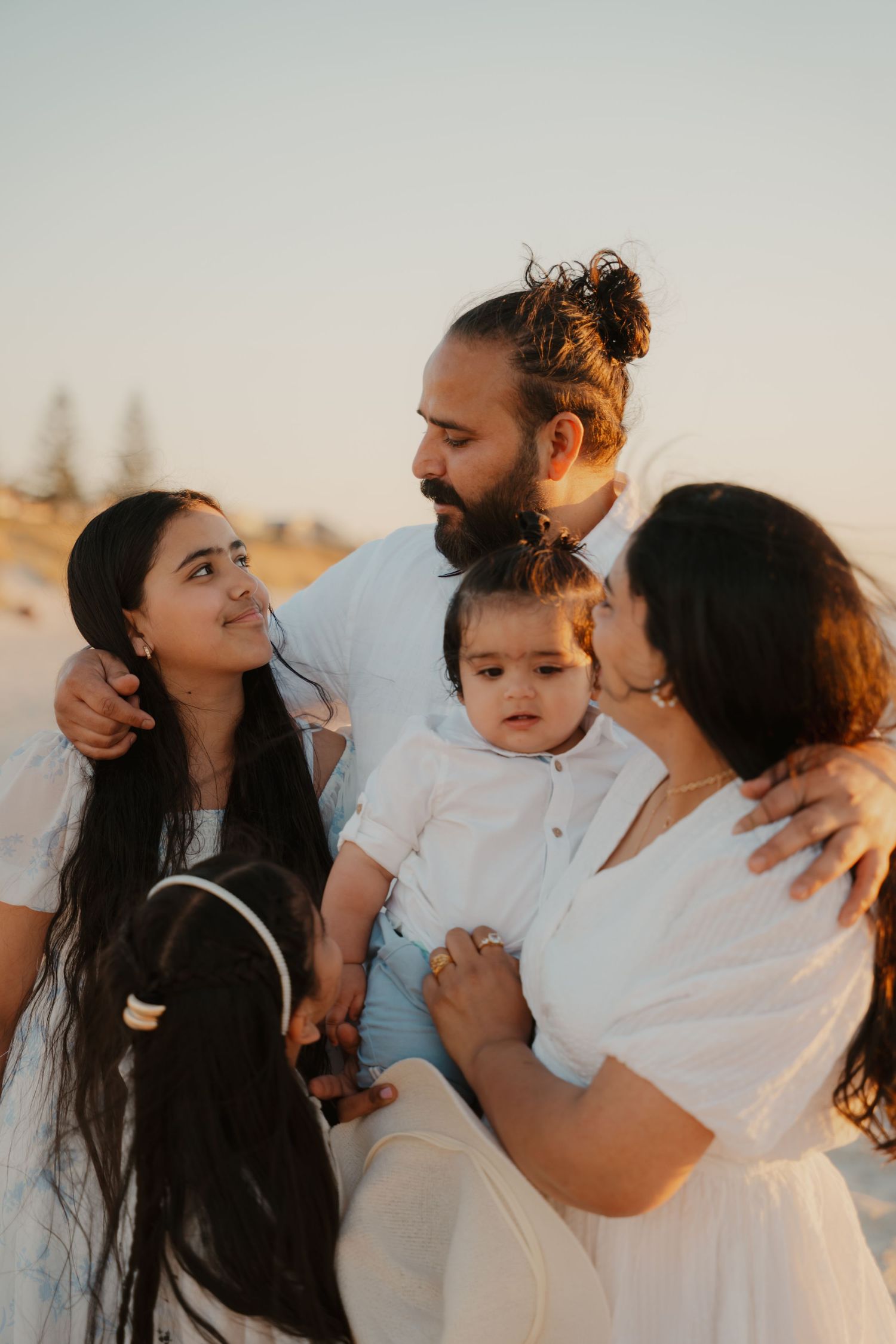 Family of five sharing a tender moment together on sandy beach during warm golden sunset.