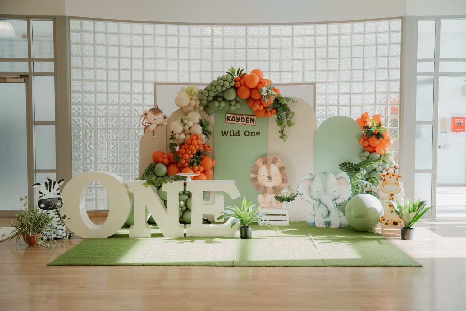 Wild One first birthday party setup with safari theme, green and orange balloon arch, and ONE letters.