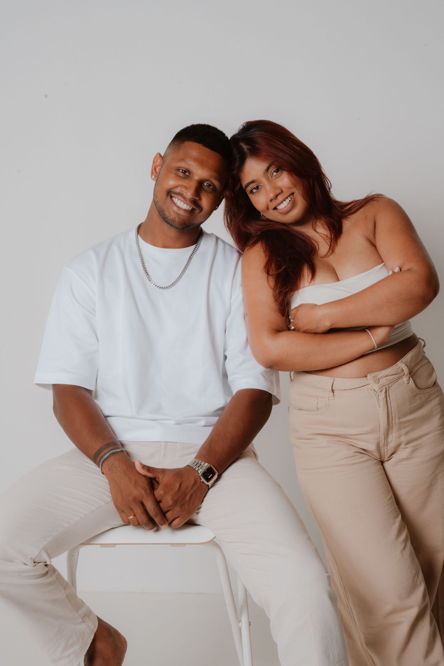 Happy couple in white and beige outfits smiling at camera in bright studio setting.