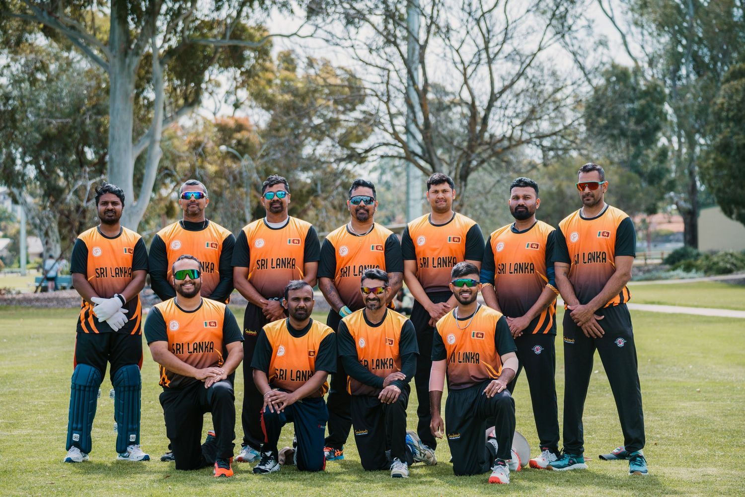 Sri Lanka cricket team poses in orange jerseys on a green field in Australia.