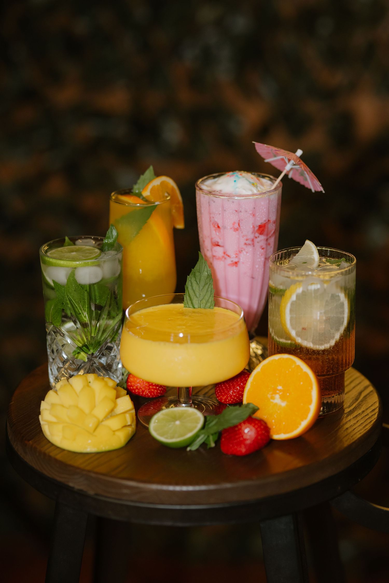 Colorful tropical cocktail spread with pineapple mango strawberry and citrus fruits on wooden table.