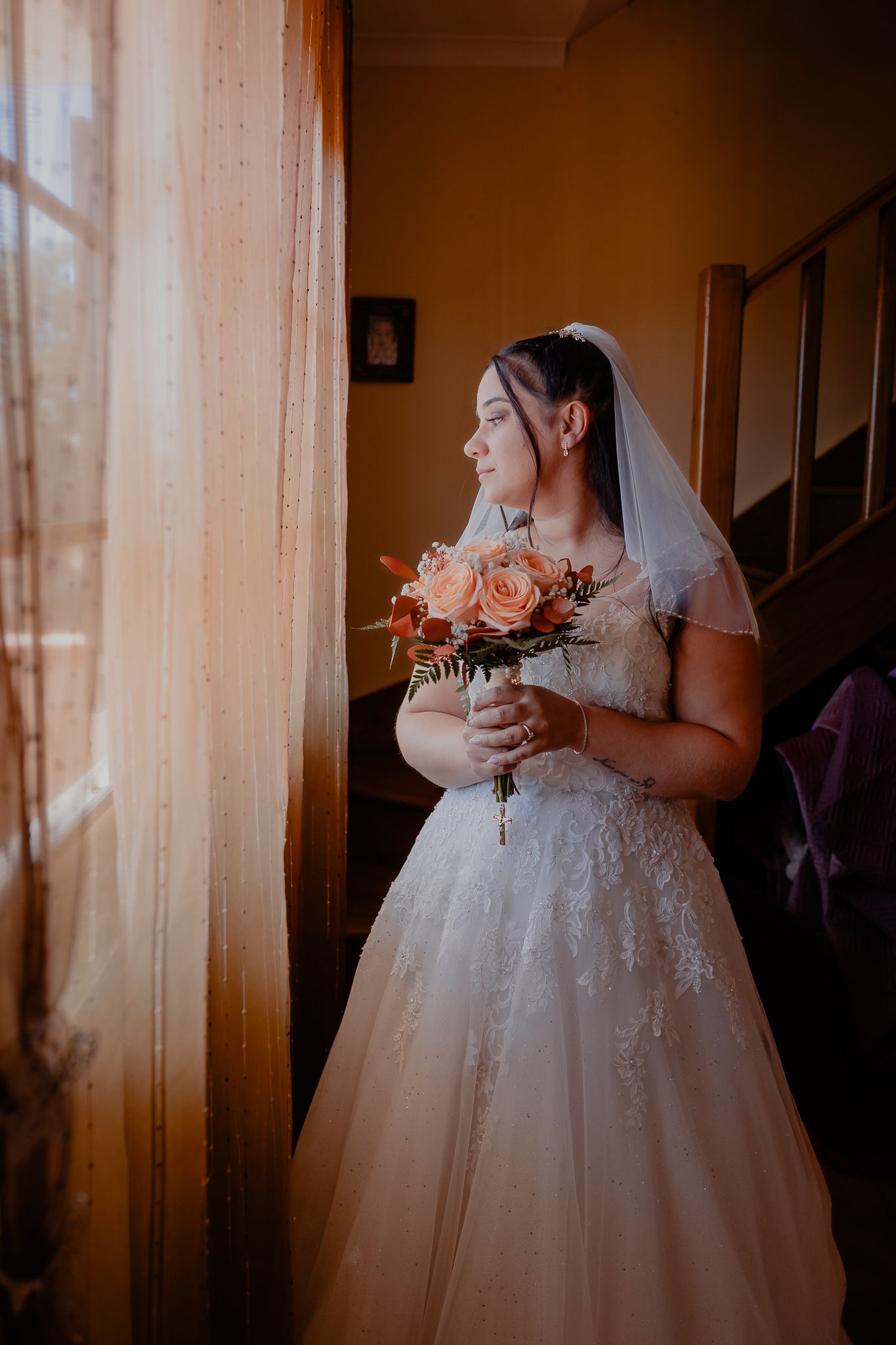 Bride in traditional white gown holding bouquet in warm interior lighting.