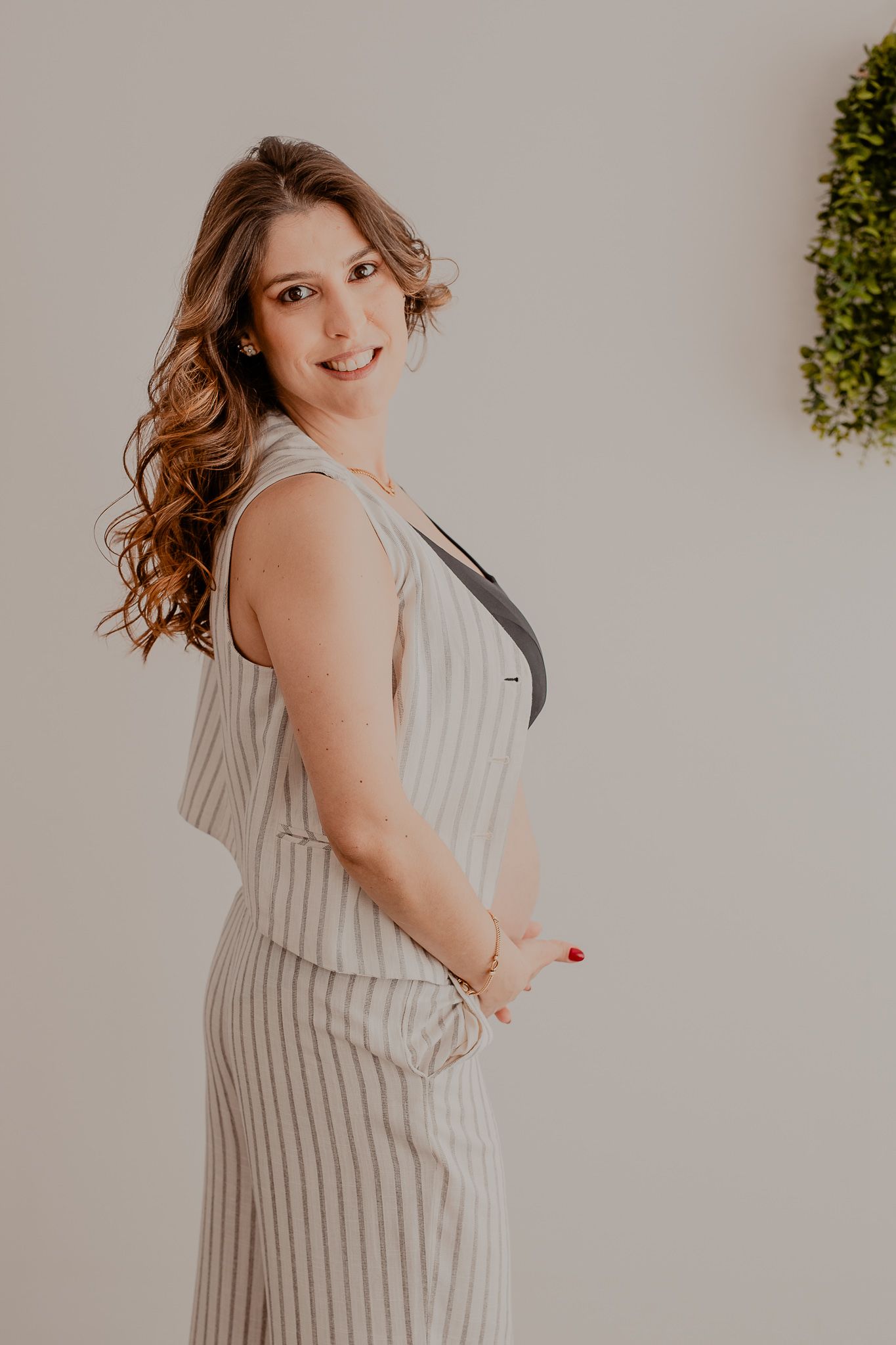 Person wearing striped dress poses against white wall with greenery decoration.