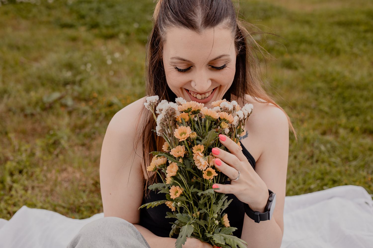 Person smelling a bouquet of peach-colored roses against a natural outdoor background.