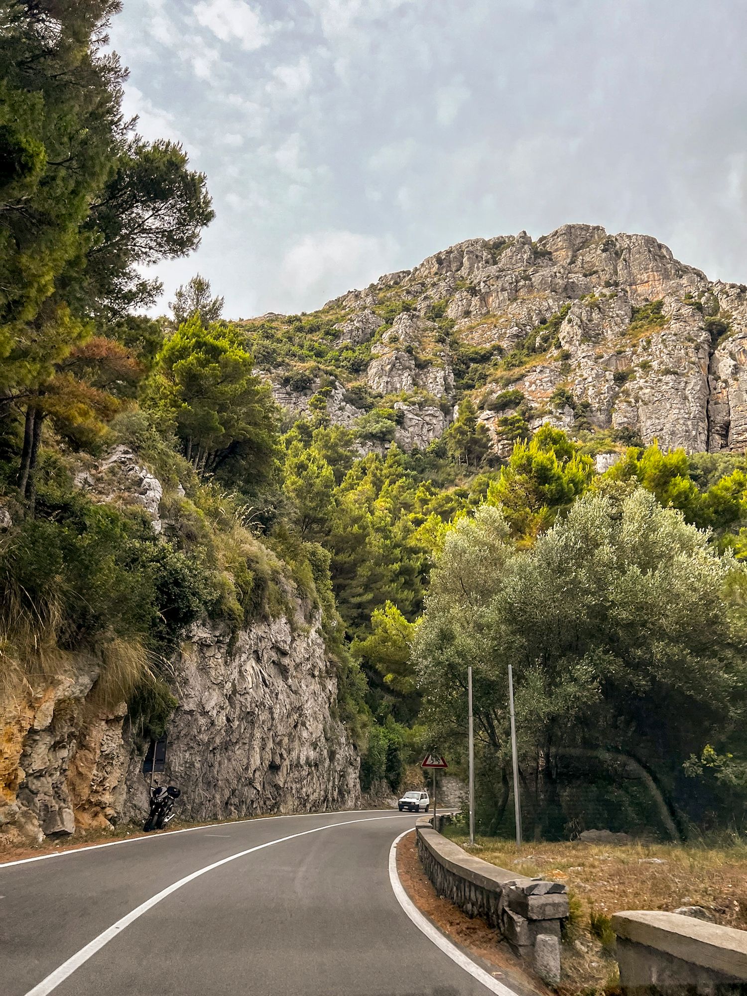 Winding mountain road curves through rocky cliffs and green vegetation in a scenic landscape.