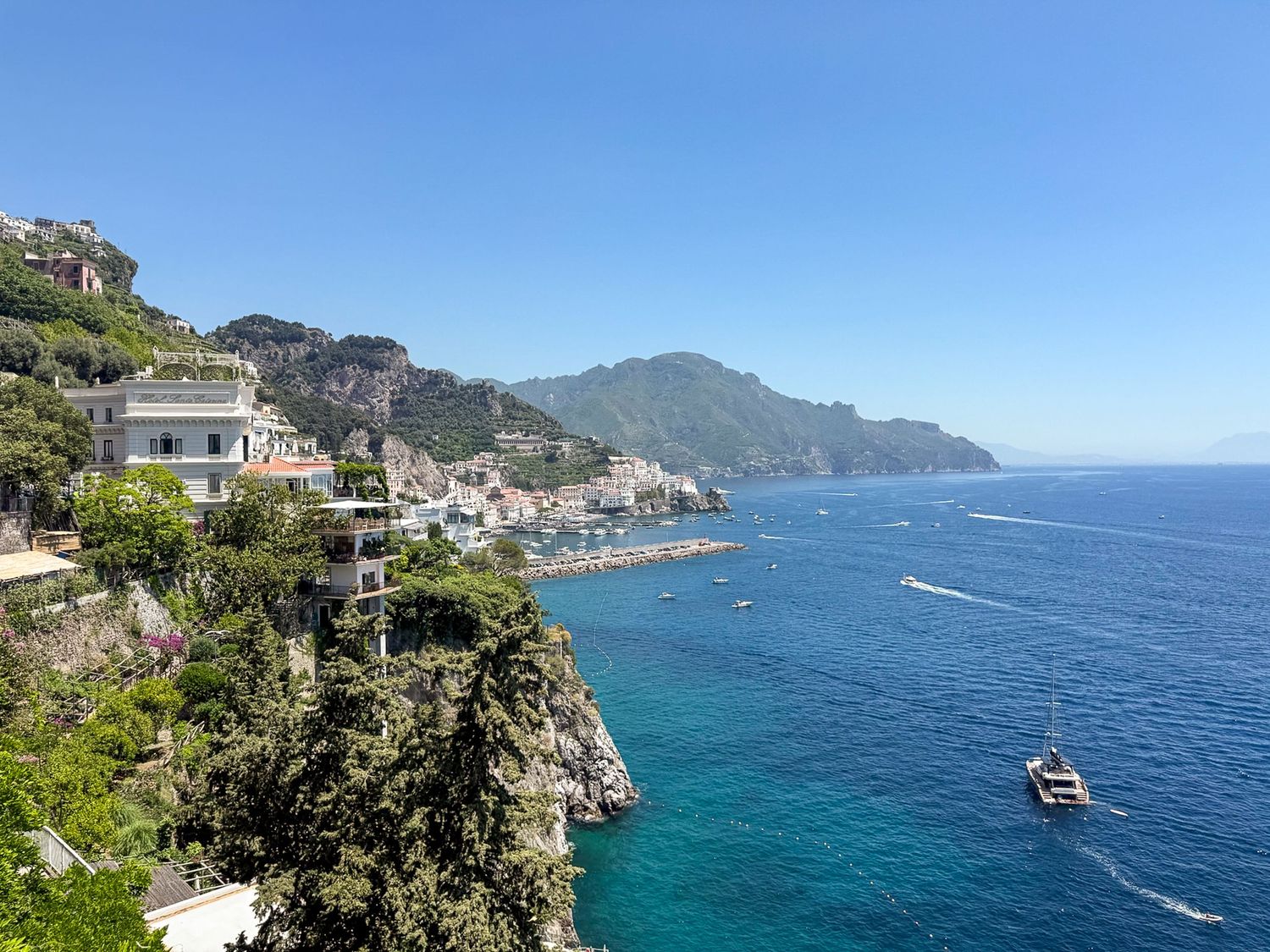 Scenic coastal view of the Amalfi Coast in Italy with colorful buildings perched on cliffs above turquoise Mediterranean waters.