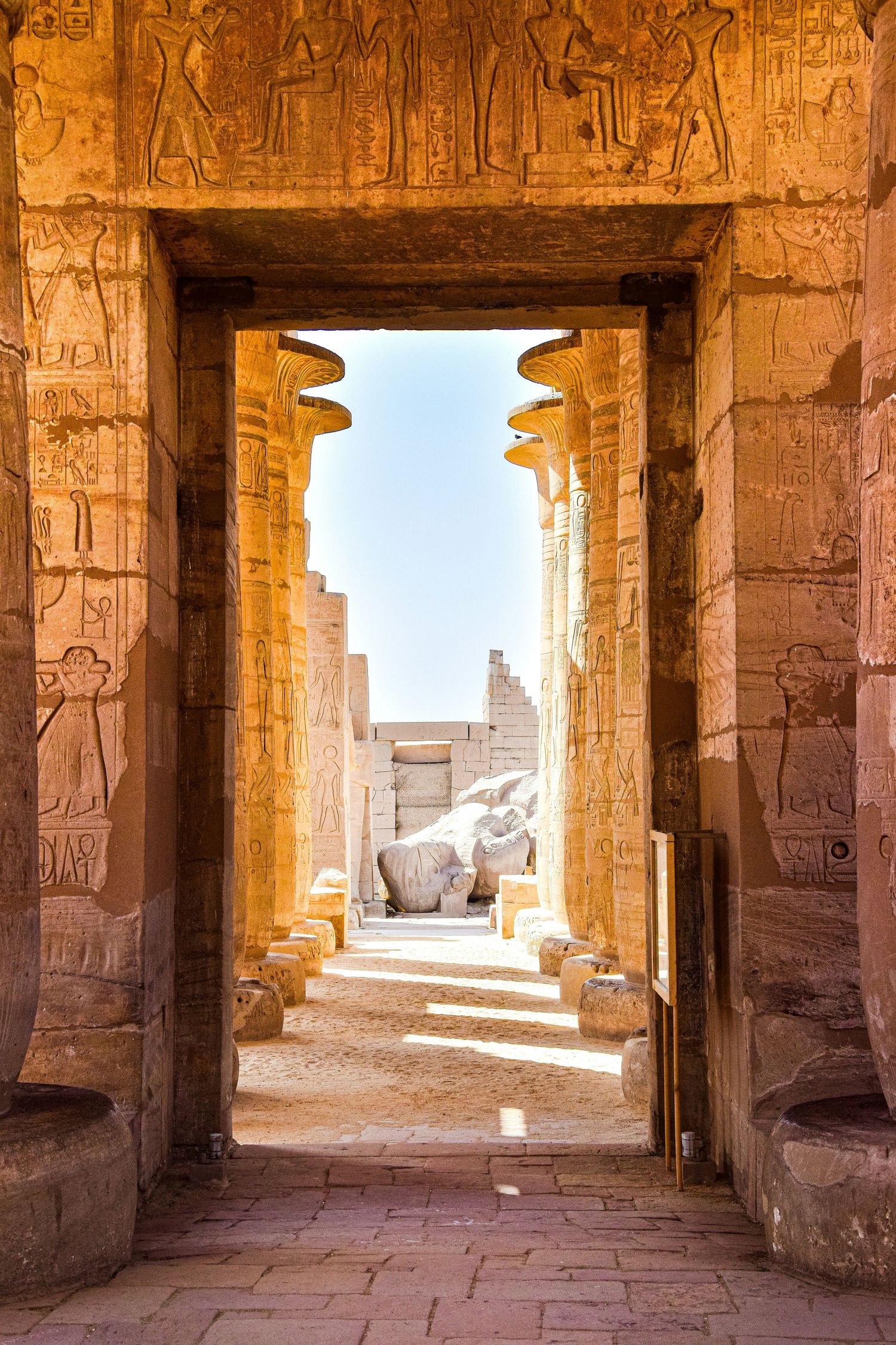 Ancient Egyptian temple doorway framing distant ruins and blue sky.