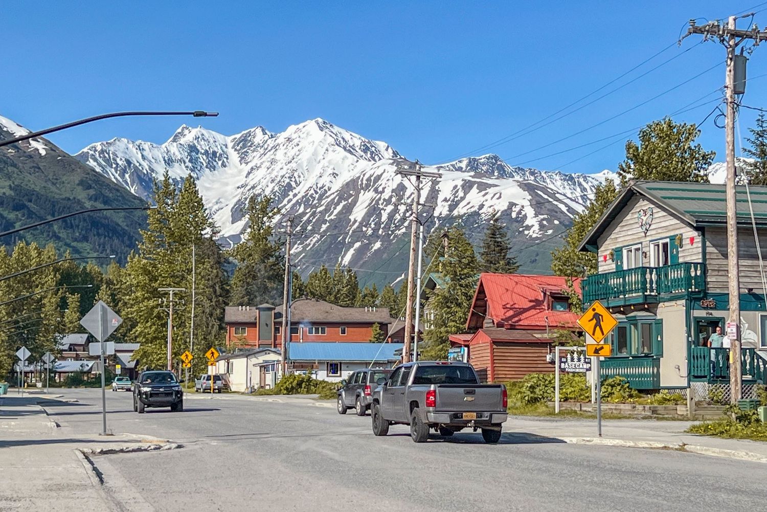 Panoramic view of a small mountain town street with snow-capped peaks rising dramatically in the background, Alaska.