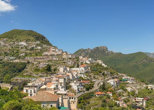 Panoramic view of colorful hillside houses and buildings in an Italian coastal village with mountains in the background.