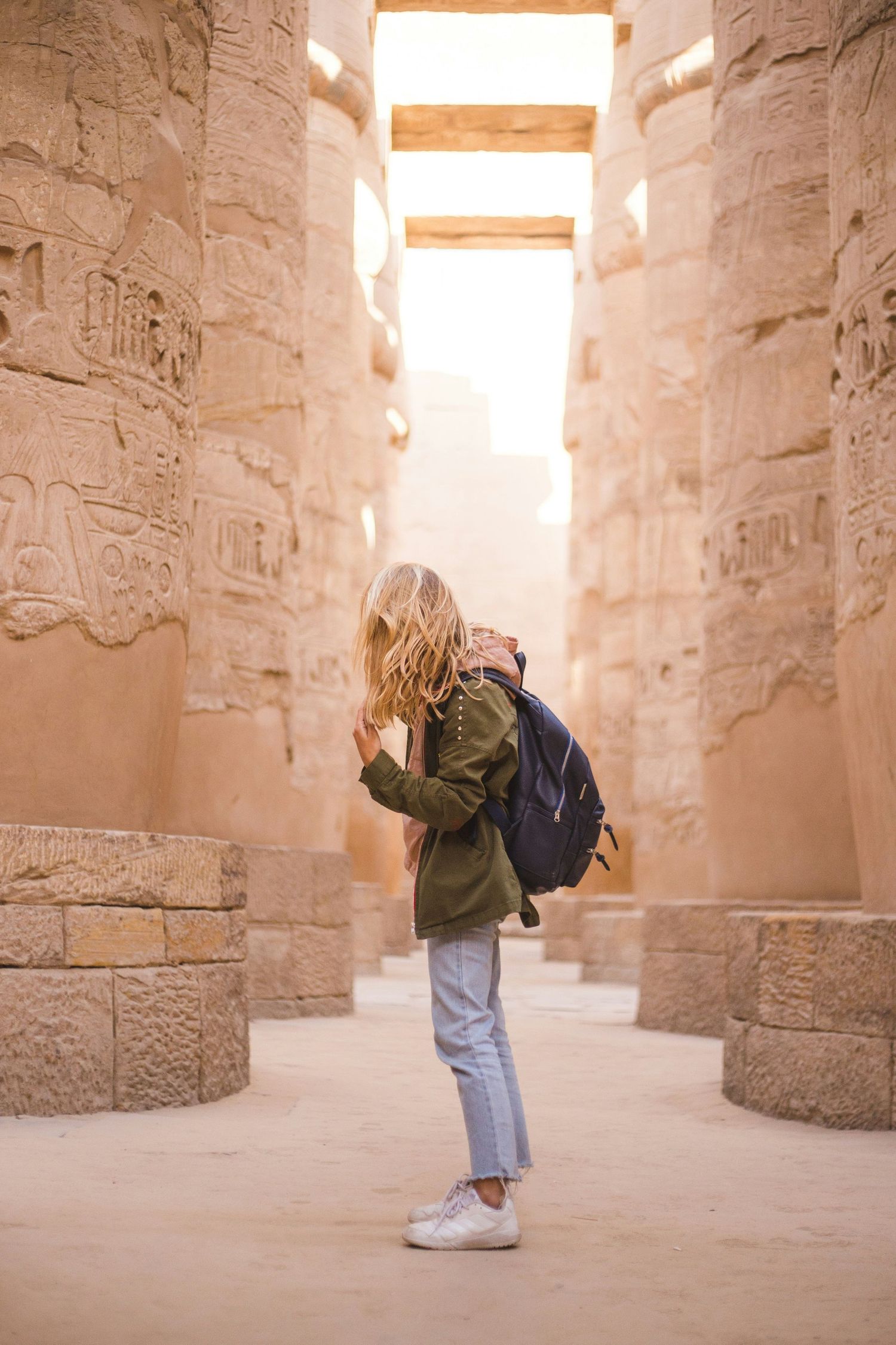 Tourist exploring ancient stone corridors of Egyptian temple with hieroglyphic-covered walls.