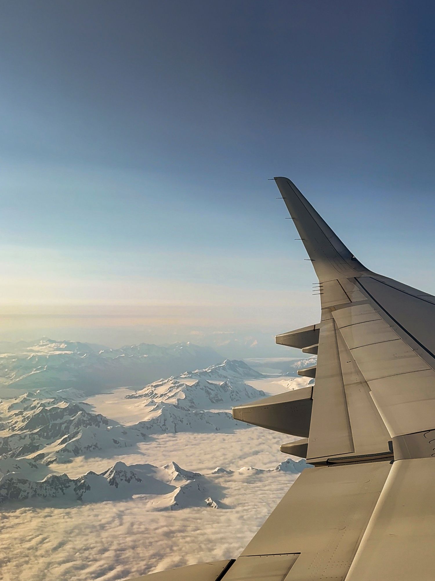 Airplane wing view over snow-covered mountains during a clear day flight.