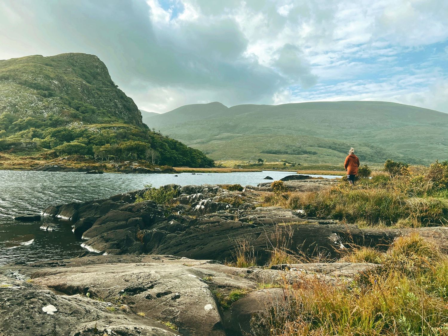 Panoramic view of rugged coastal cliffs and grassy hills along the Irish coastline under dramatic cloudy skies.