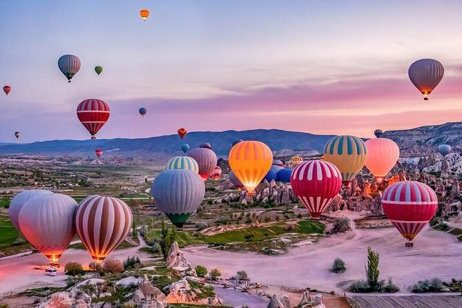 Colorful hot air balloons float over scenic Cappadocia landscape during sunrise.