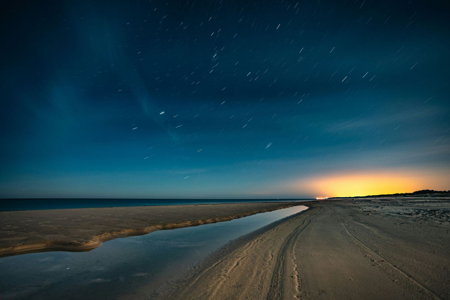 Night sky panorama over a desert landscape with stars and fading sunset on the horizon.