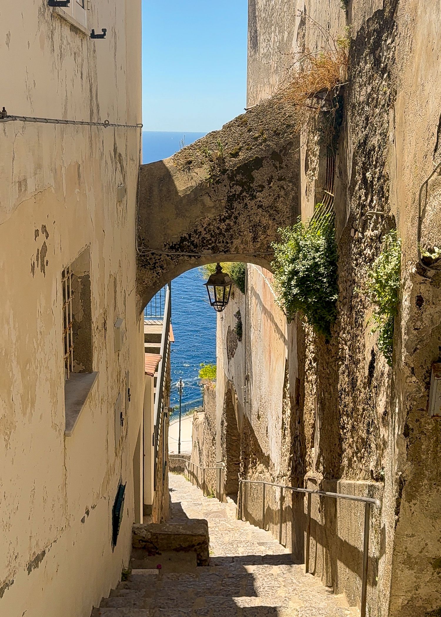 Narrow stone alleyway leading to ocean view between whitewashed walls.