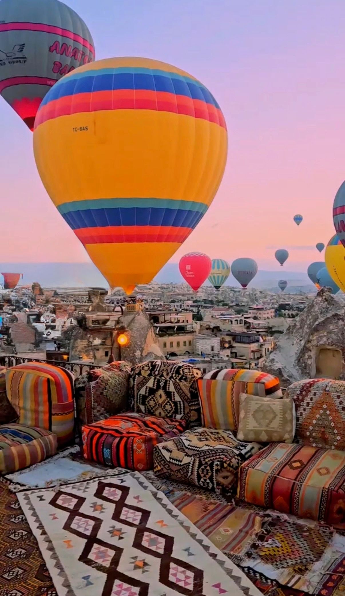 Colorful hot air balloons floating over Cappadocia with traditional Turkish cushions in foreground.