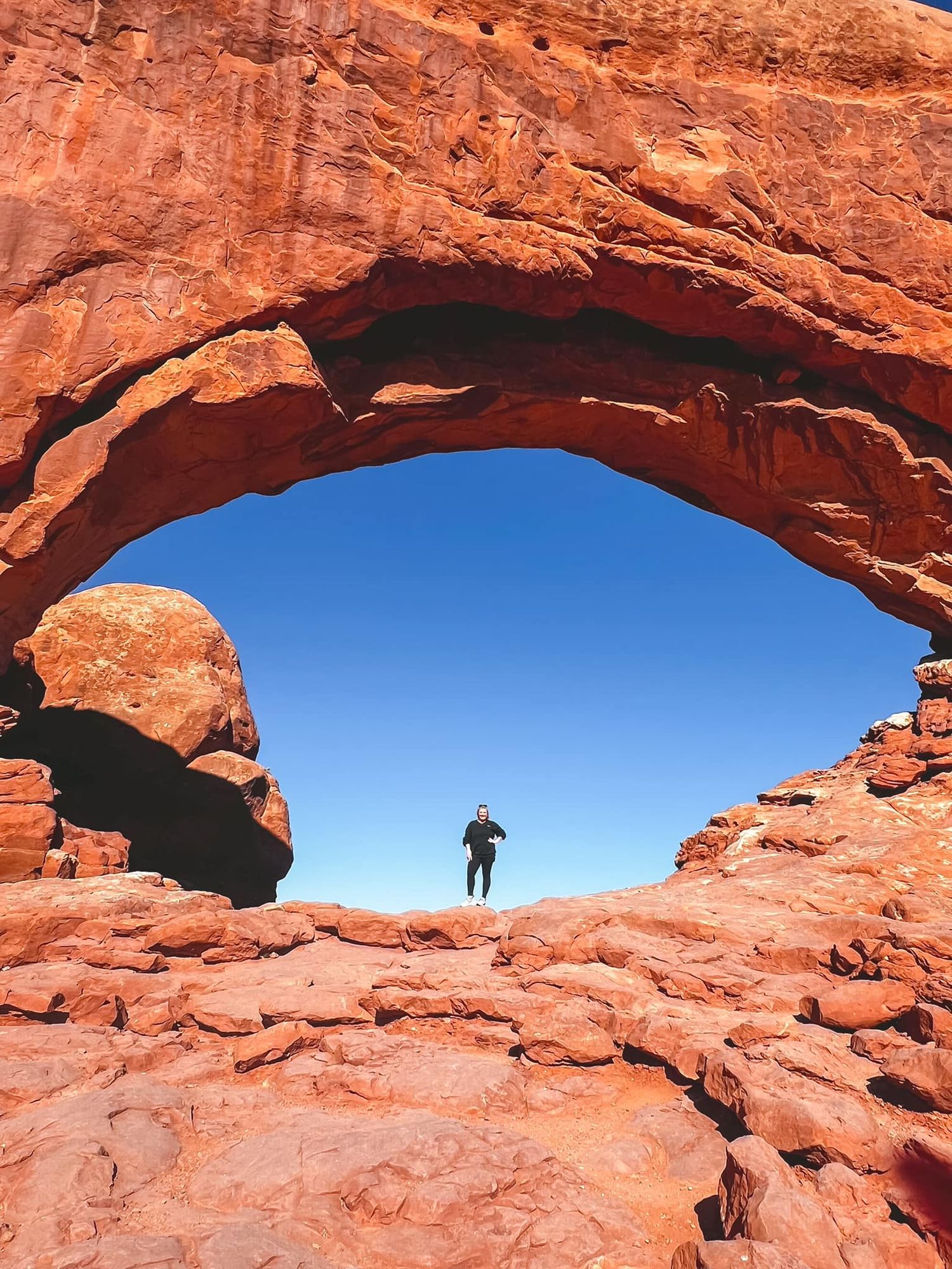 Natural rock arch formation in red sandstone against bright blue desert sky.