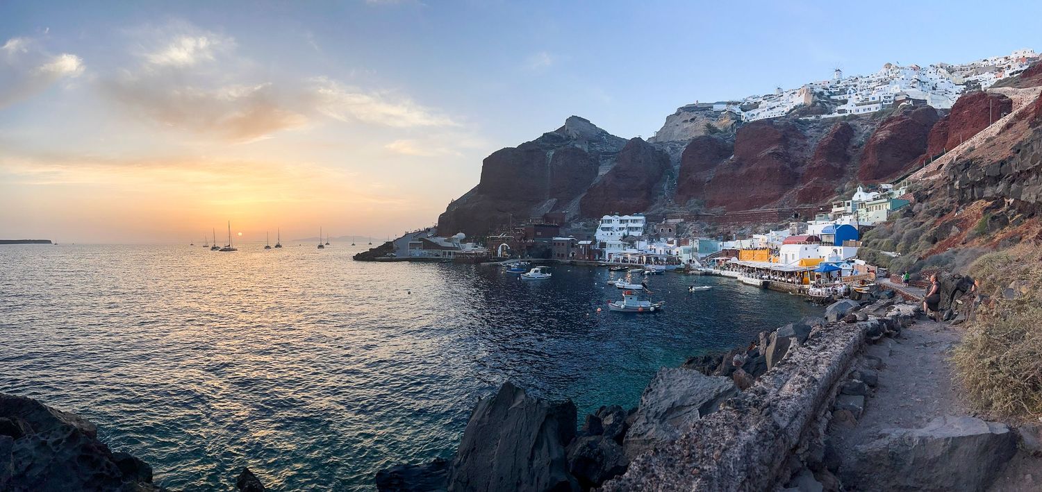 Dramatic coastal sunset views with rocky cliffs and Mediterranean buildings along the coastline.