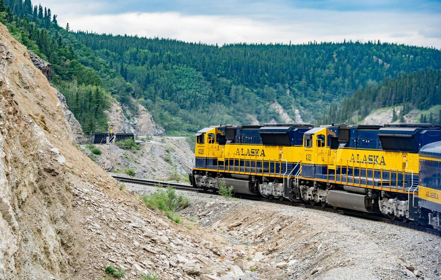 Yellow and blue Alaska Railroad train winding through a mountainous landscape.