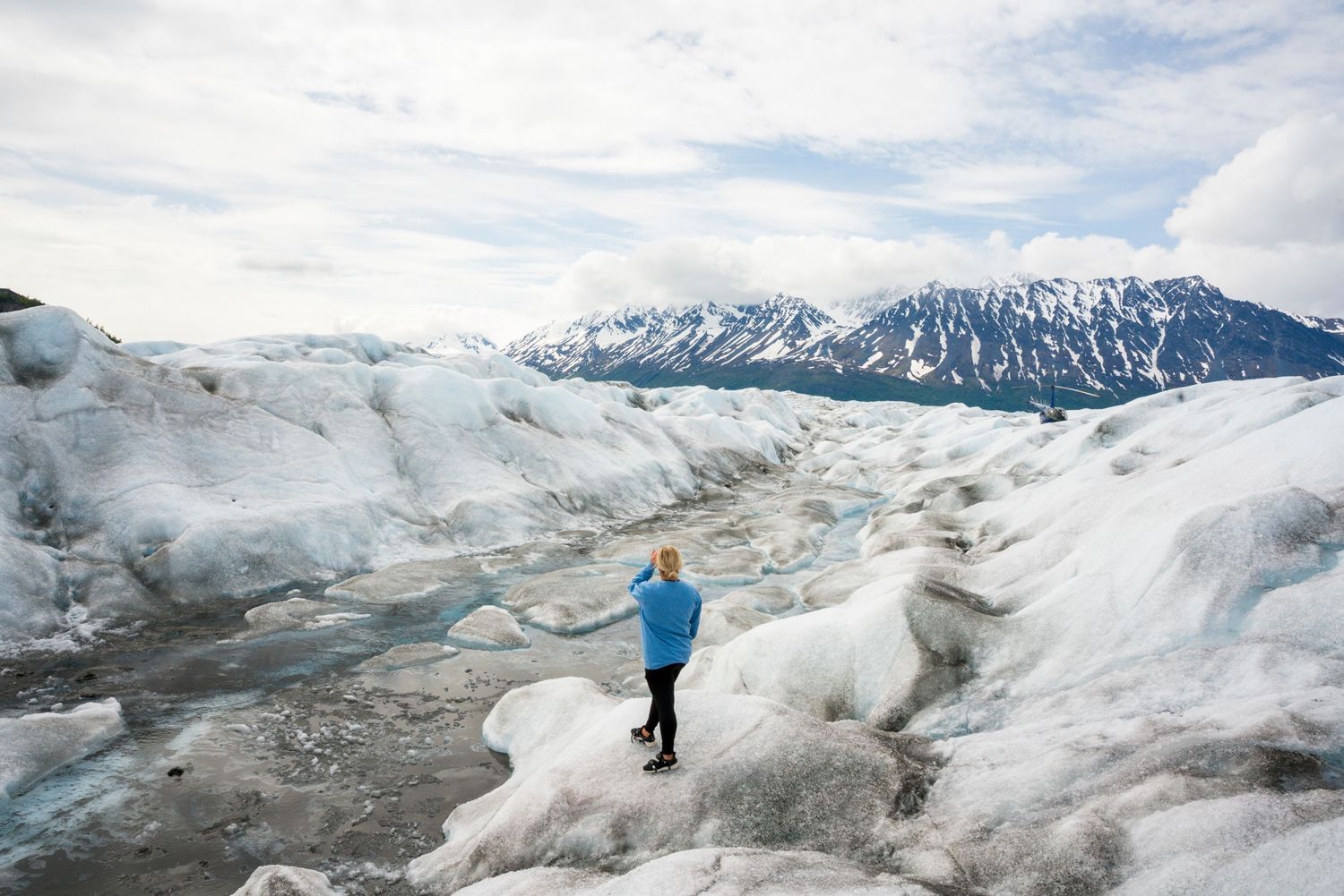 Hikers exploring the vast white and blue terrain of a glacier landscape surrounded by mountain peaks.