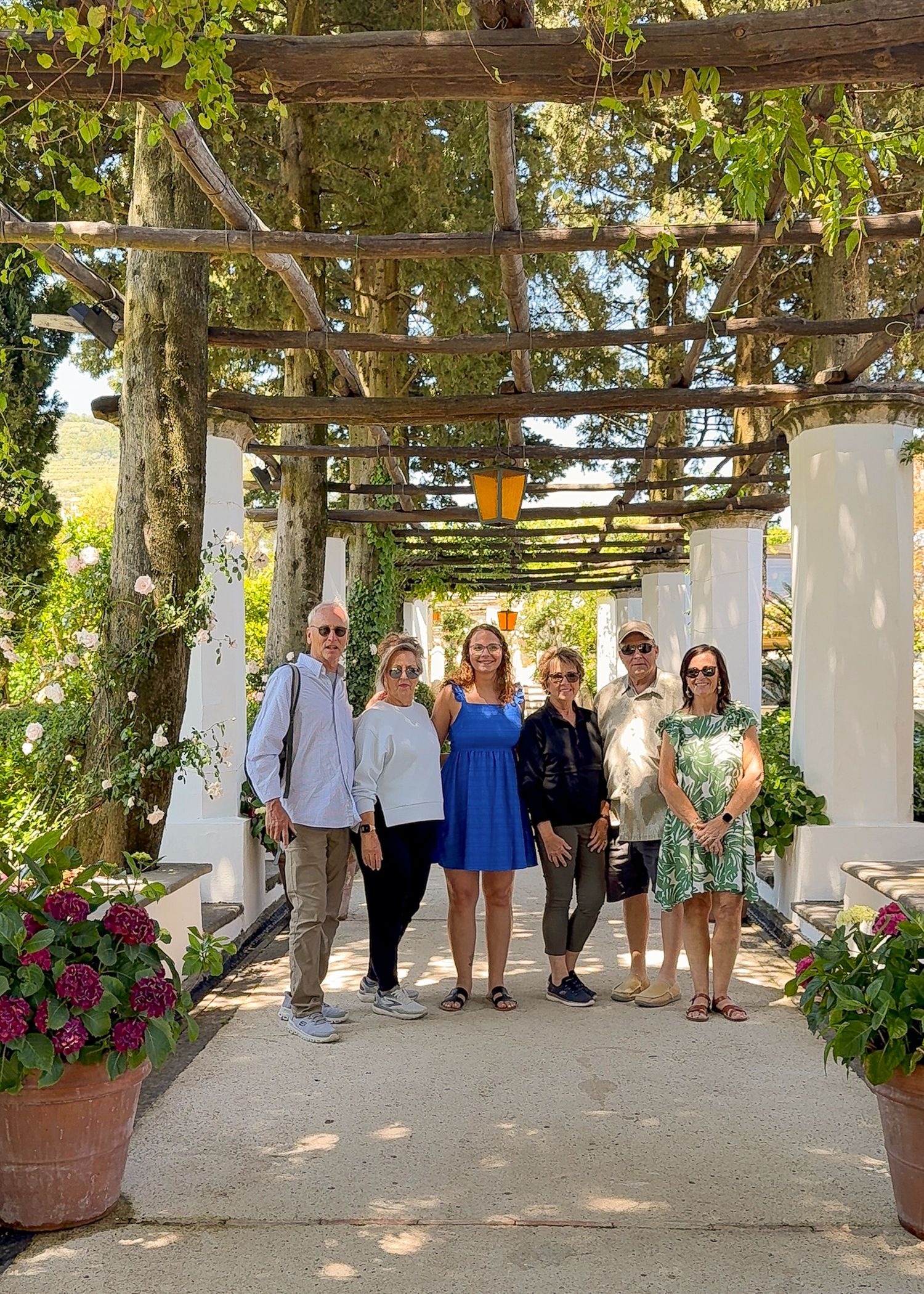 Tour group standing under a rustic wooden pergola decorated with climbing plants and flowers.