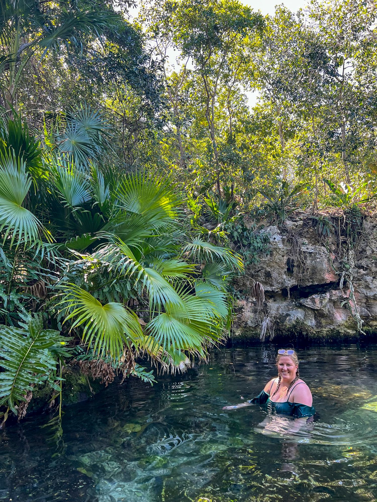 Scenic tropical cenote surrounded by lush palm fronds and limestone walls in Mexico's Yucatan peninsula.