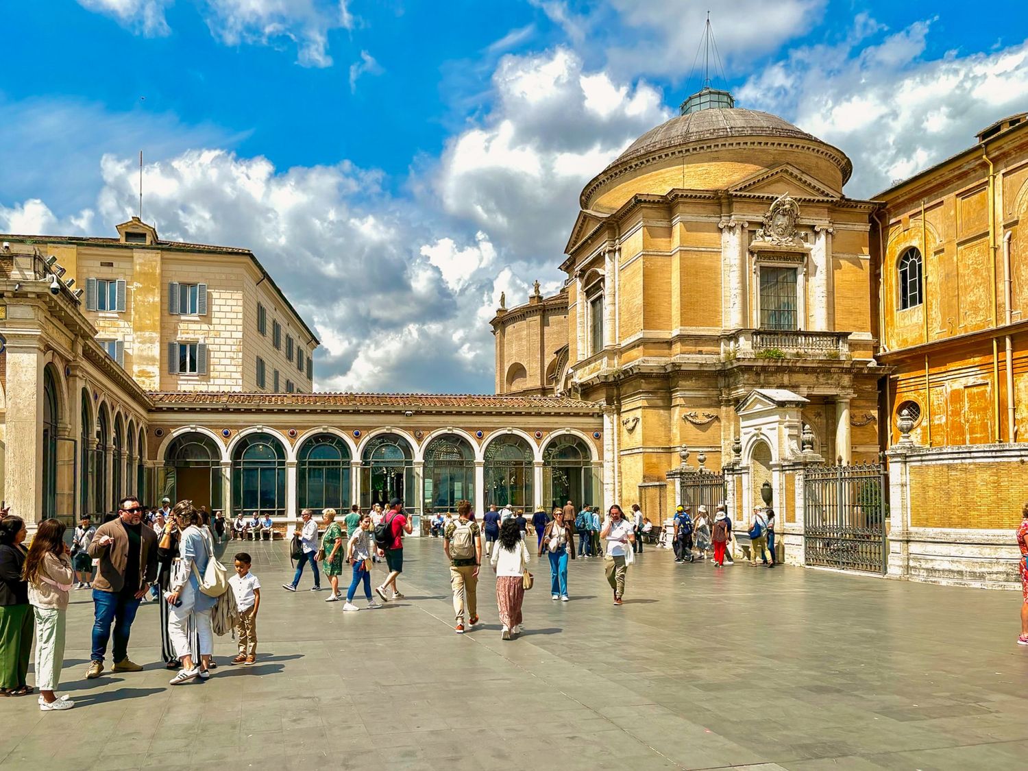 Panoramic view of St. Peter's Square with crowds of tourists and classical architecture.