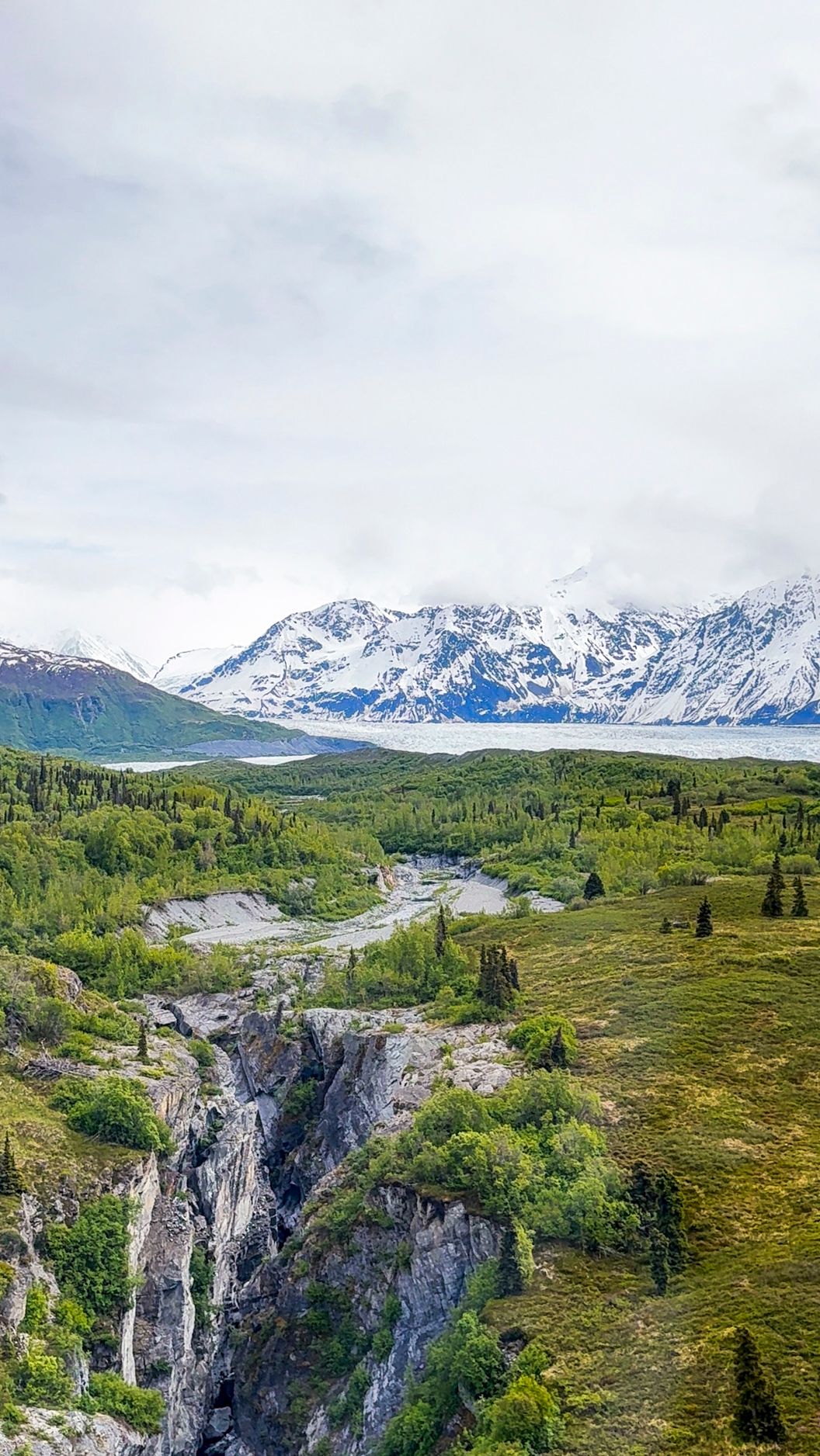 Mountain landscape with deep canyon, green valley, and snow-capped peaks in the distance.