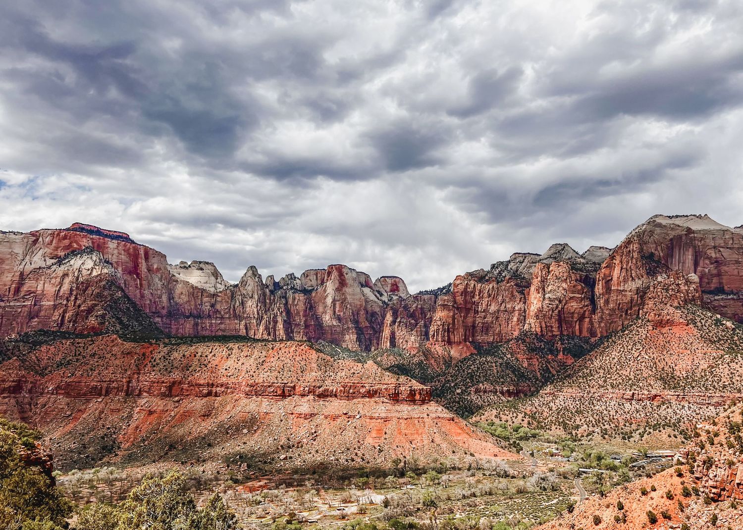 Panoramic vista of red rock canyon formations under dramatic cloudy skies in Utah.