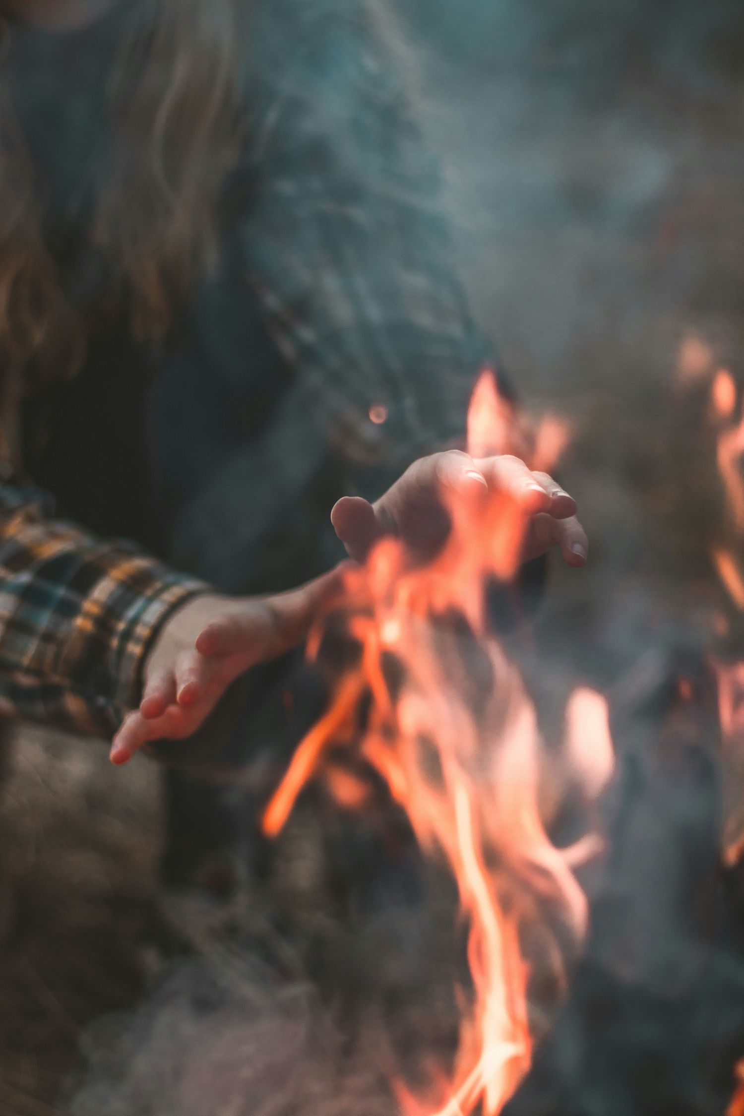 Hands warming by glowing orange campfire flames at dusk.