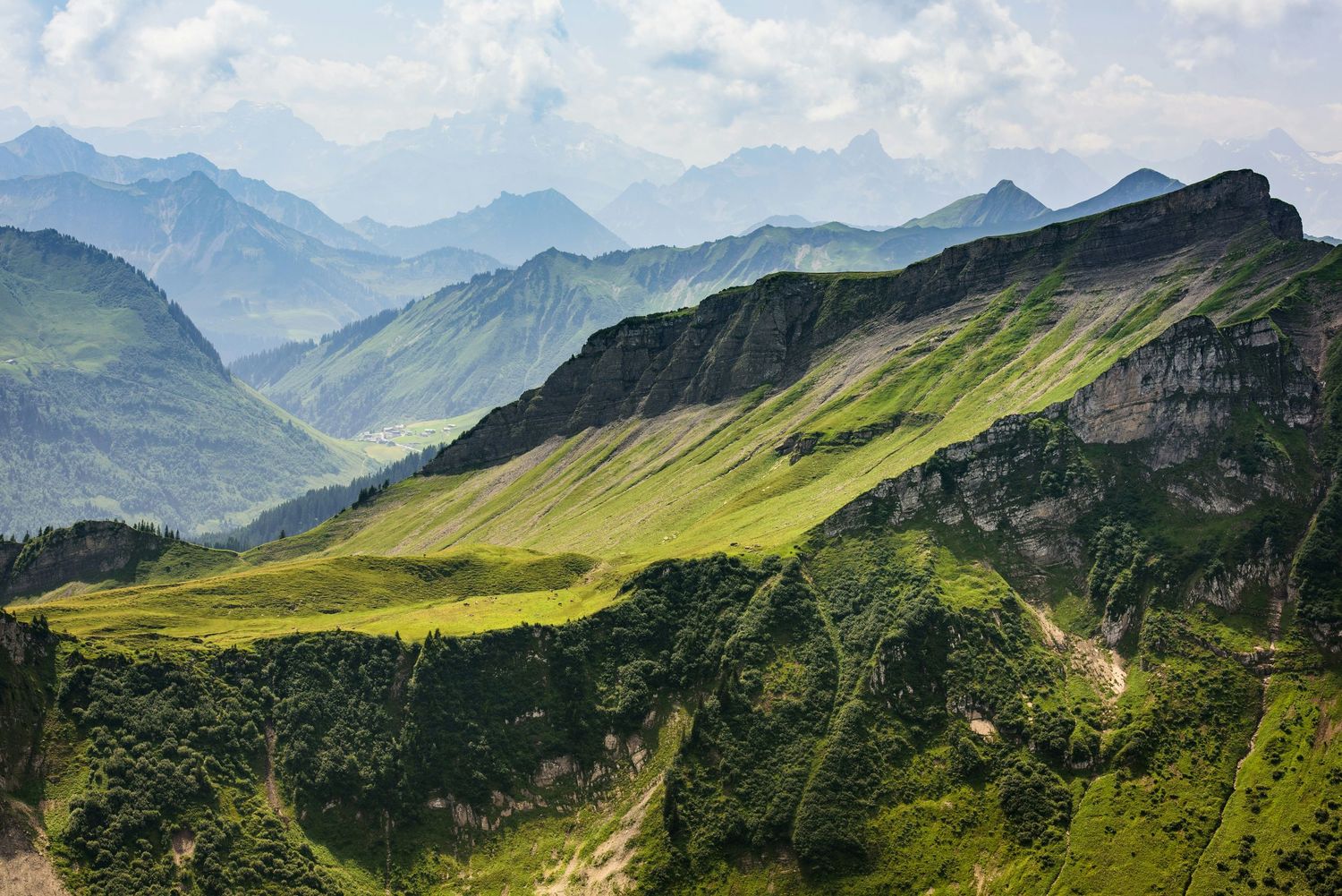 Dramatic mountain landscape with lush green valleys and peaks under blue skies in the Alps.